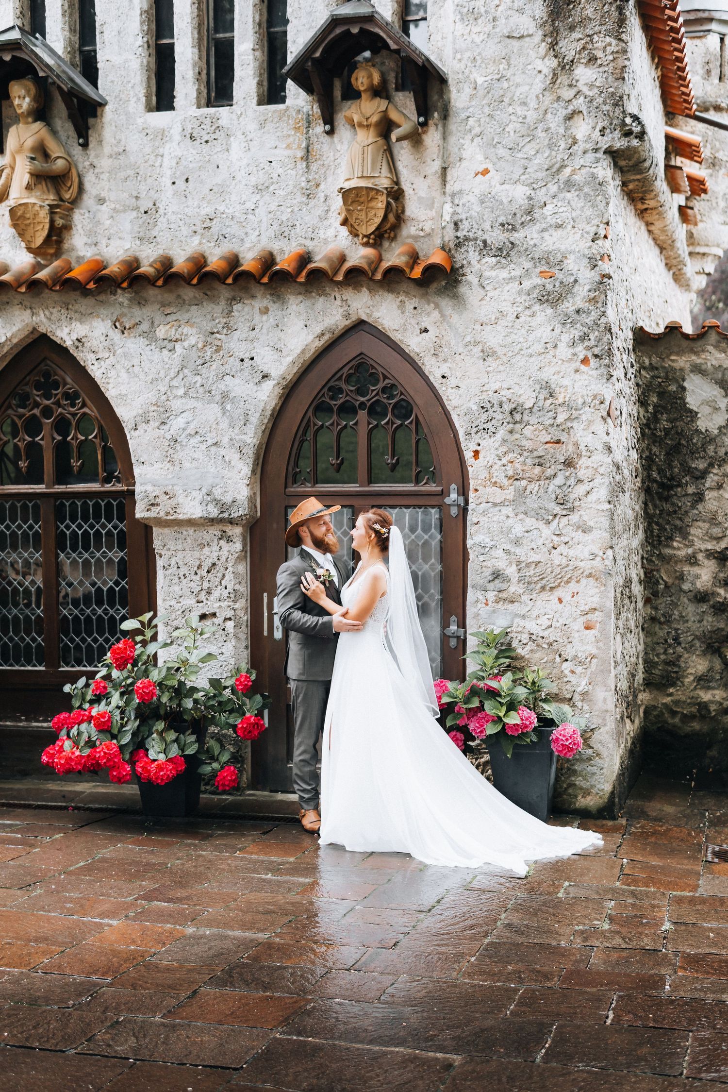 A romantic wedding moment against a rustic stone wall with arched doorways and blooming red roses.