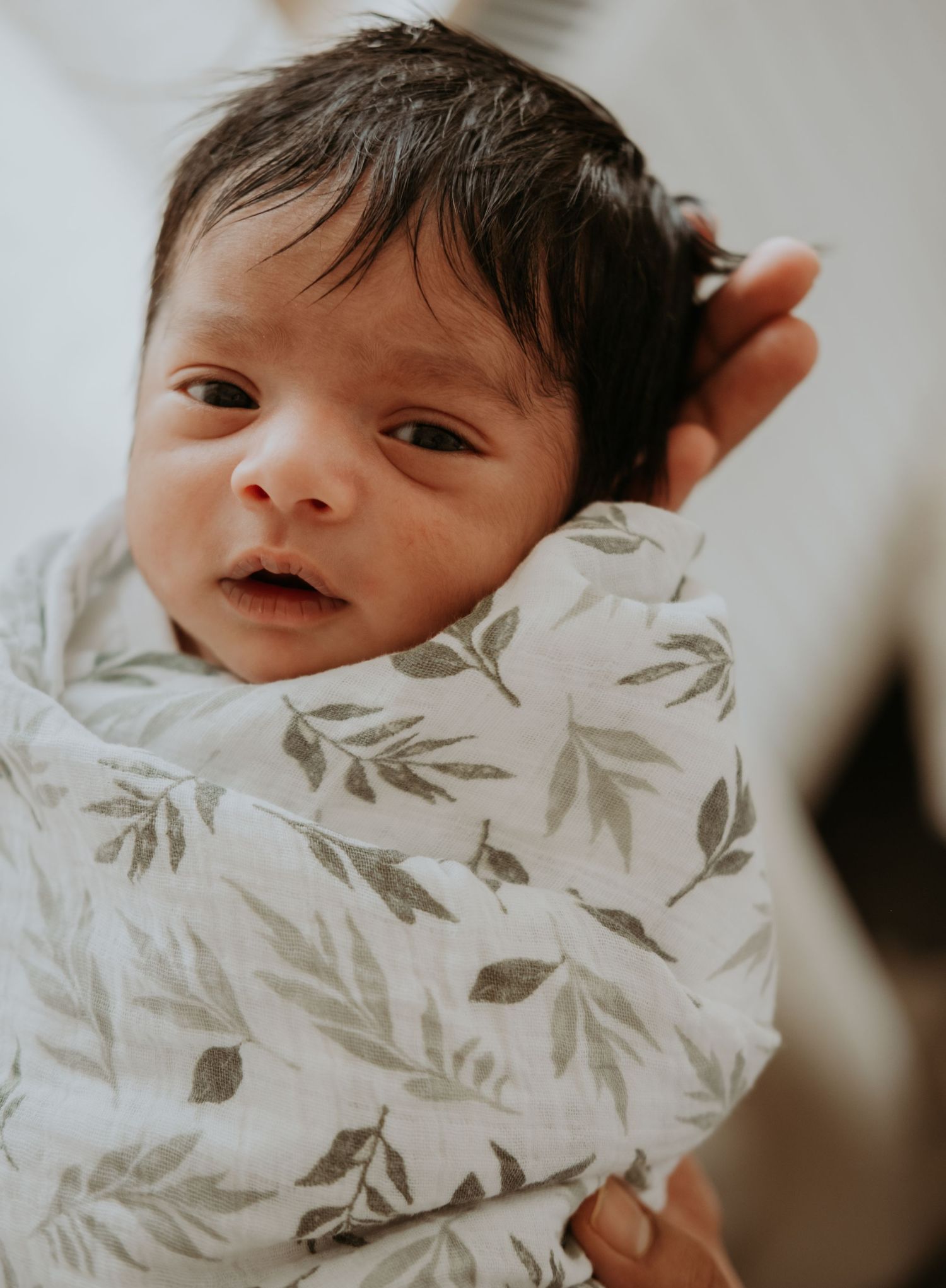 A baby lies on a white blanket with delicate gray leaf patterns, creating a soft and dreamy nursery scene.