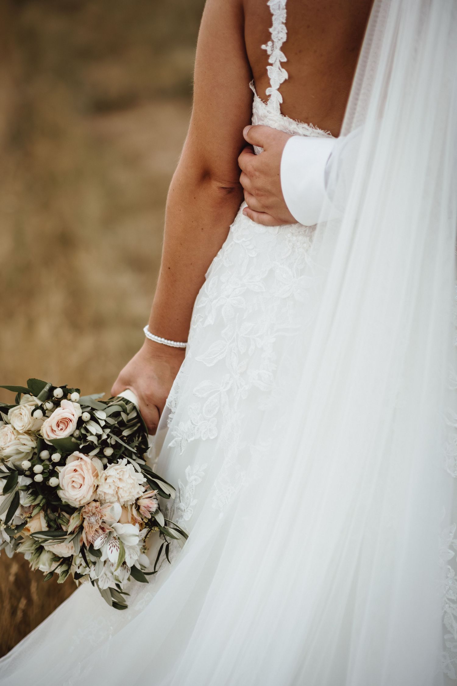Delicate wedding bouquet with blush roses and greenery held against a white tulle wedding dress.