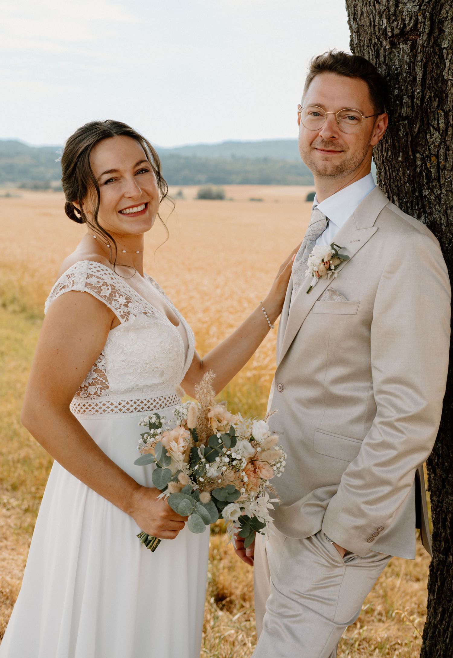 A couple in white wedding attire embrace in a golden wheat field during a romantic countryside photo session.