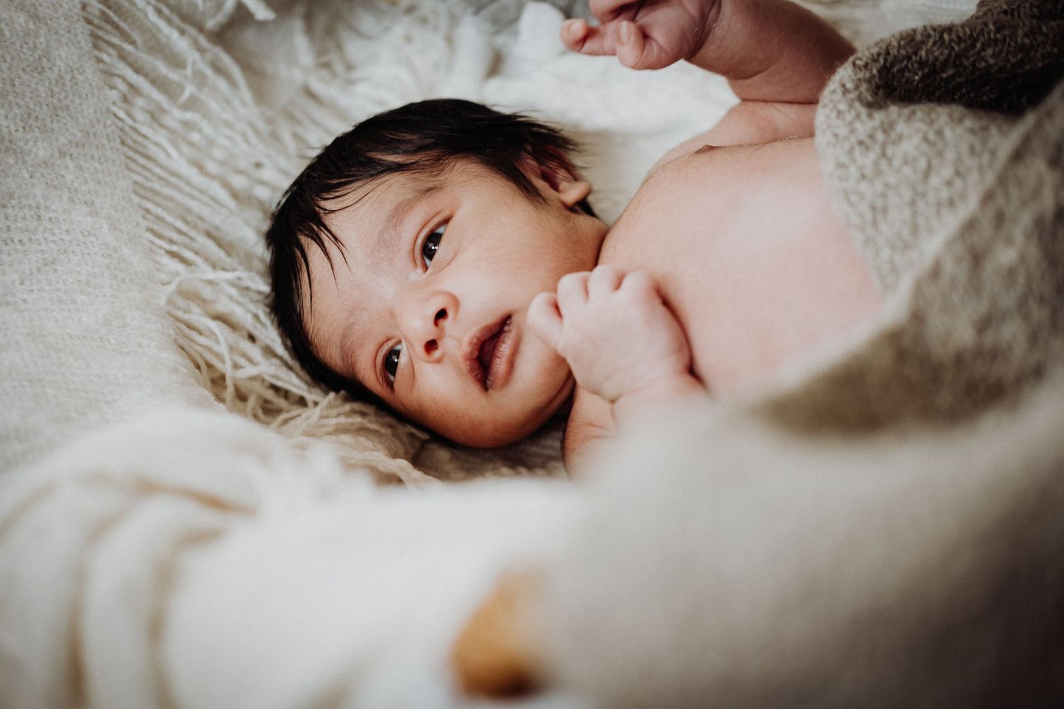 A smiling baby lies on white bedding surrounded by soft blankets.