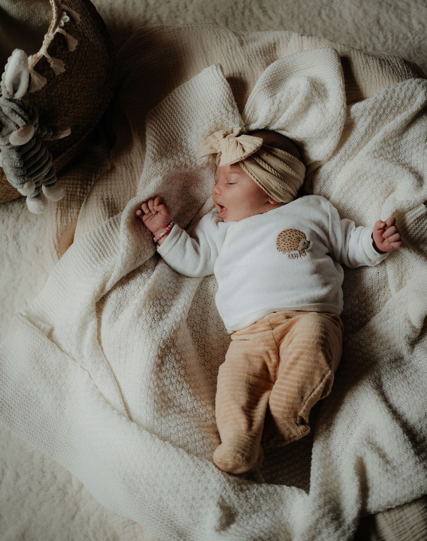 Baby sleeping peacefully on white bedding while wearing a cream-colored outfit.