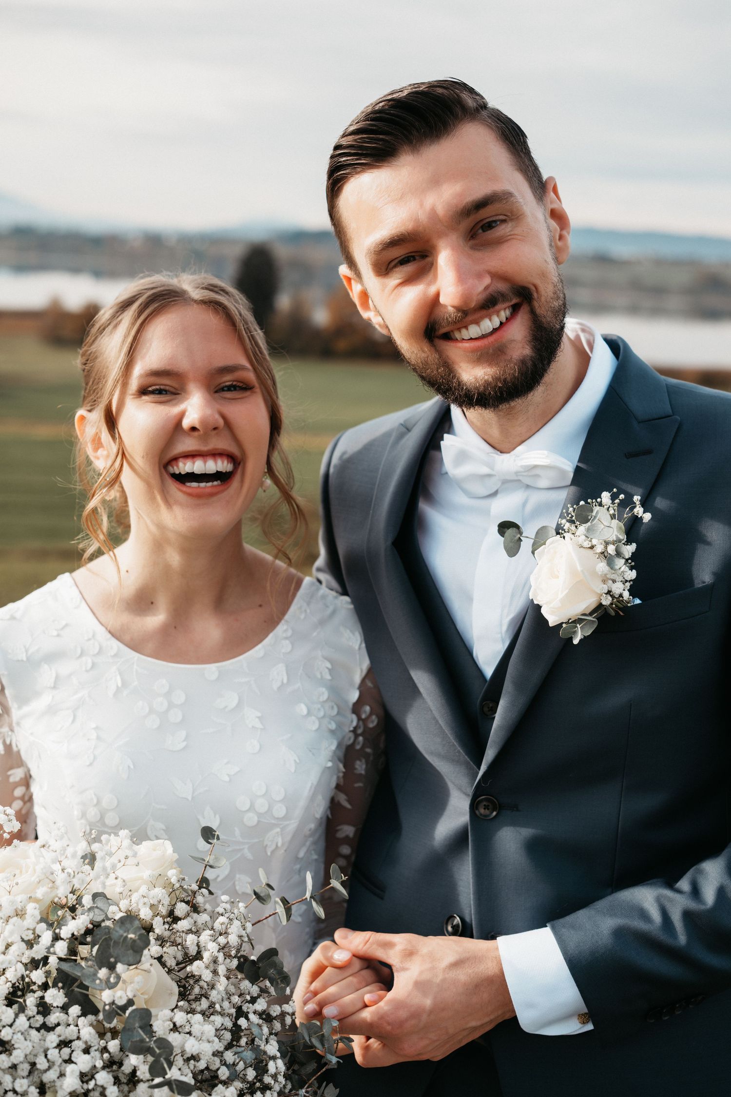 A joyful wedding couple shares candid moments together in a series of outdoor portraits with white floral bouquet details.
