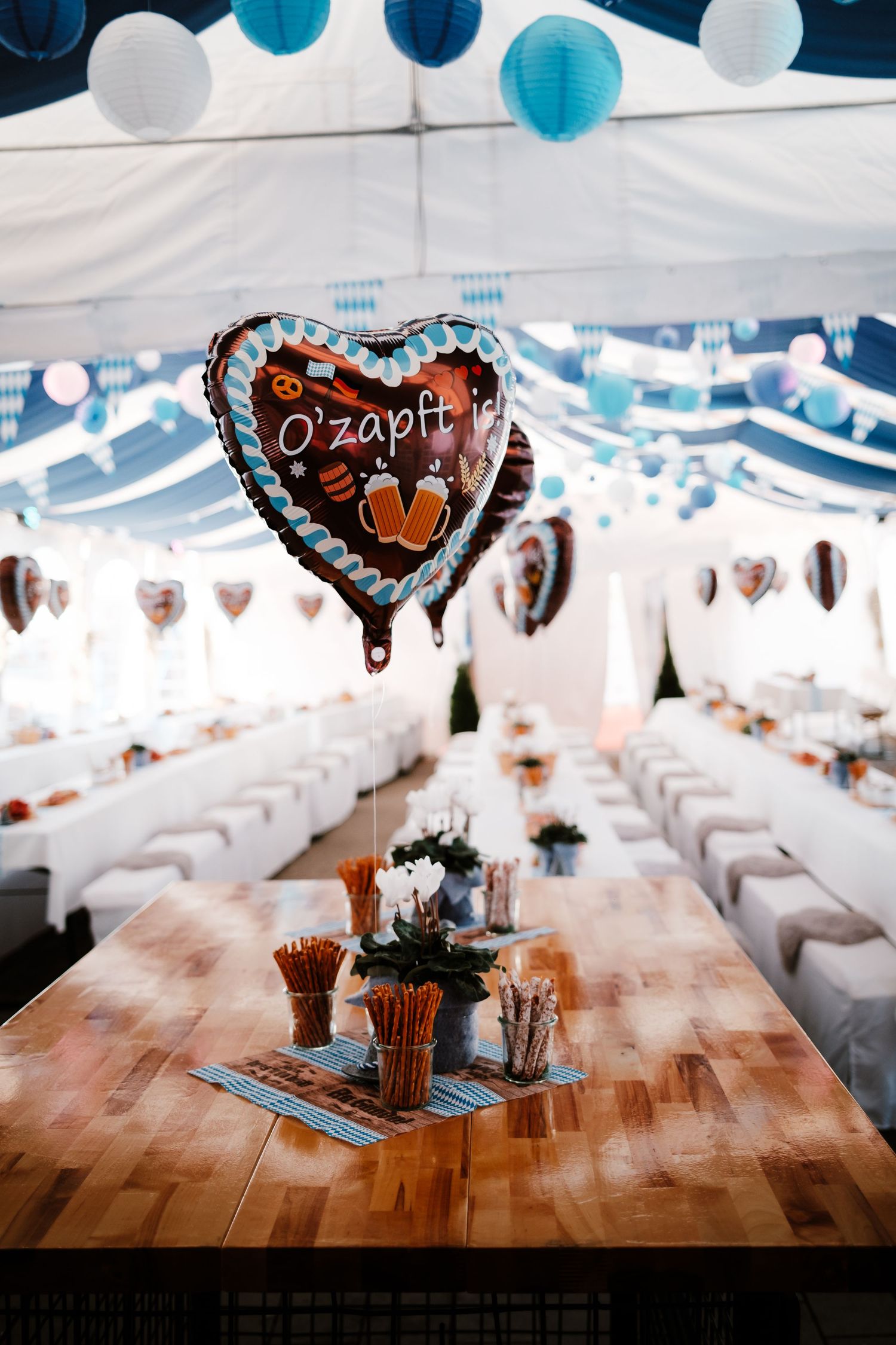 Wedding reception tables decorated with blue balloons and heart-shaped decor under a white tent canopy.
