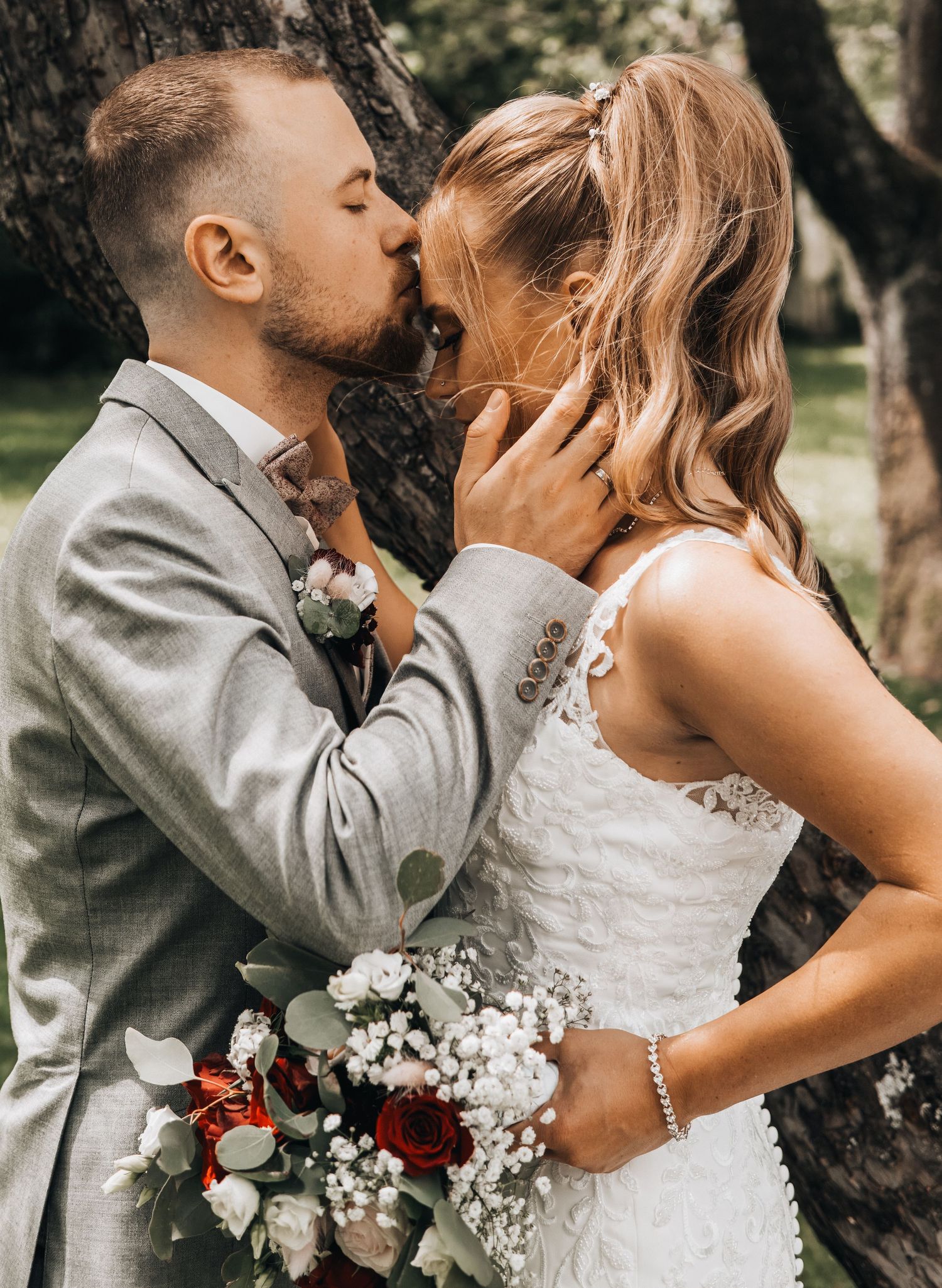 A romantic wedding couple shares intimate kisses in a series of outdoor photos with natural lighting and white flowers.