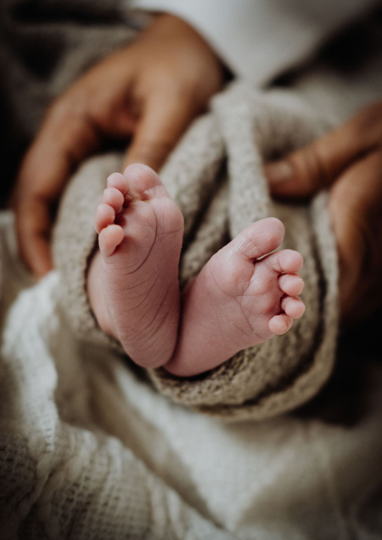 Close-up sequence of tiny newborn baby feet resting on a soft beige knit blanket.