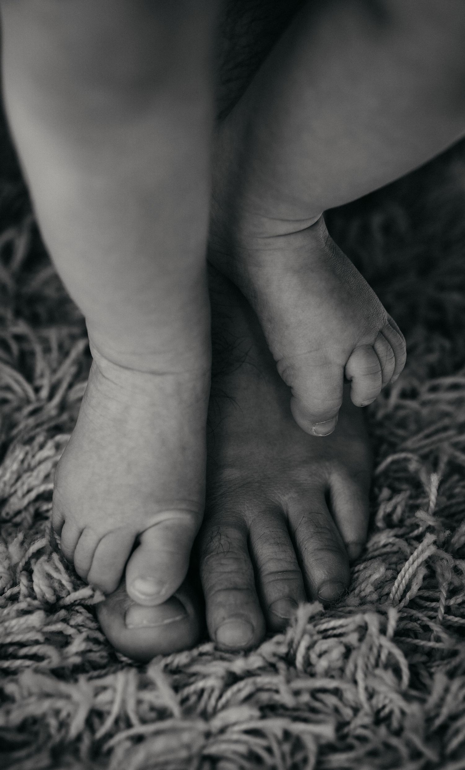 Black and white close-up of small bare feet standing on a textured carpet or rug.