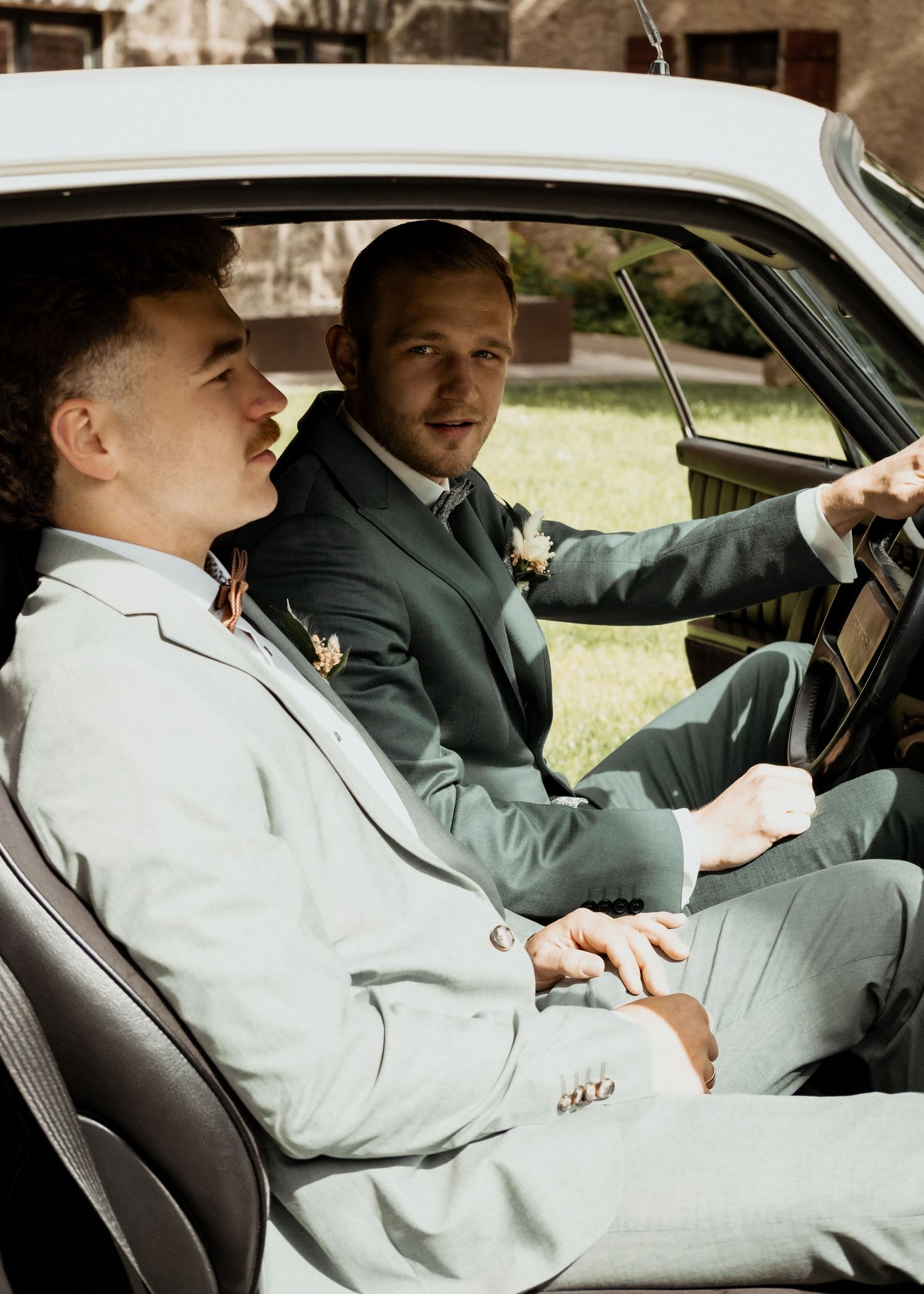 Two people in formal attire sit in a car interior having a conversation during what appears to be a special occasion.