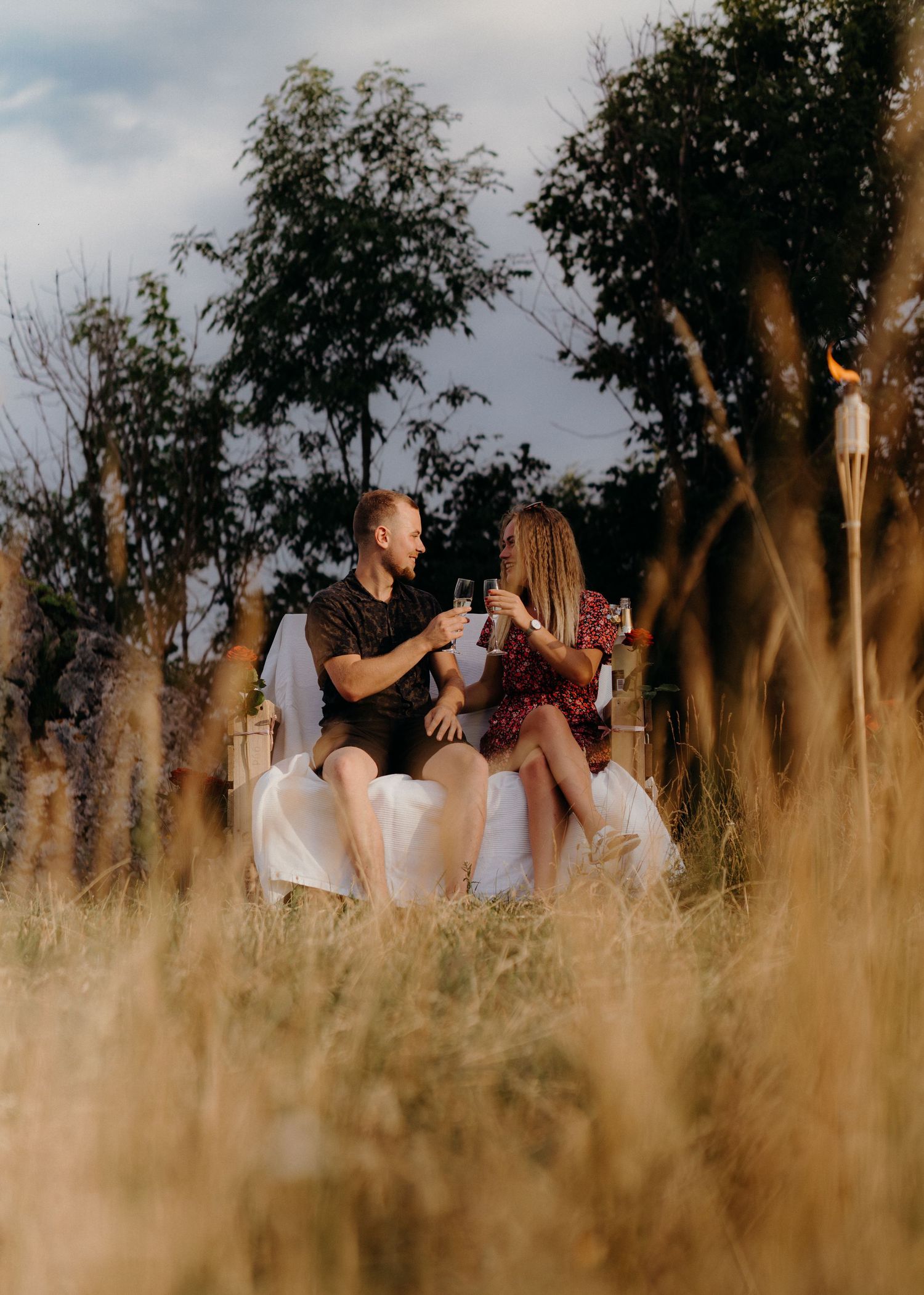A couple shares a romantic moment in a golden wheat field during sunset with trees in the background.