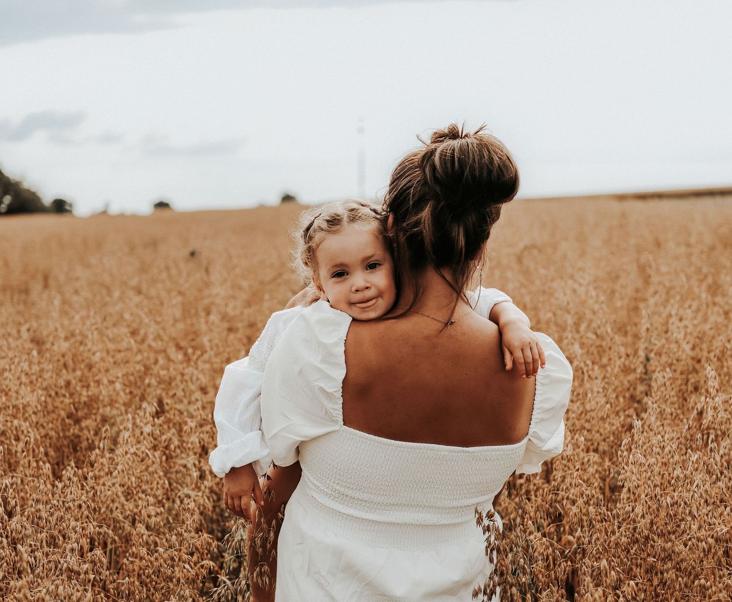 Romantic couple embraces in a golden wheat field during sunset, bride wearing a flowing white dress.