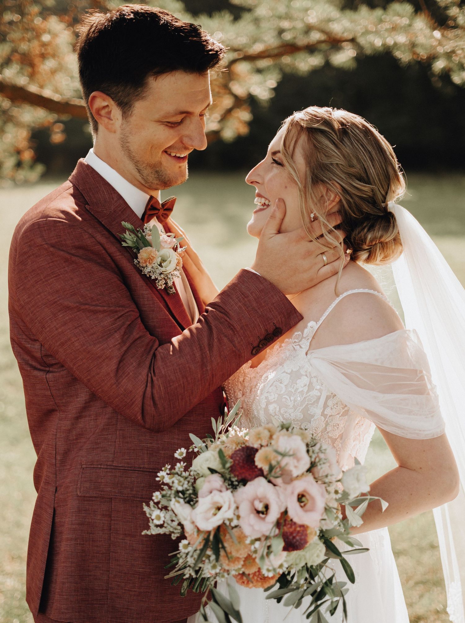 Romantic wedding portrait with couple in burgundy suit and white dress holding floral bouquet.