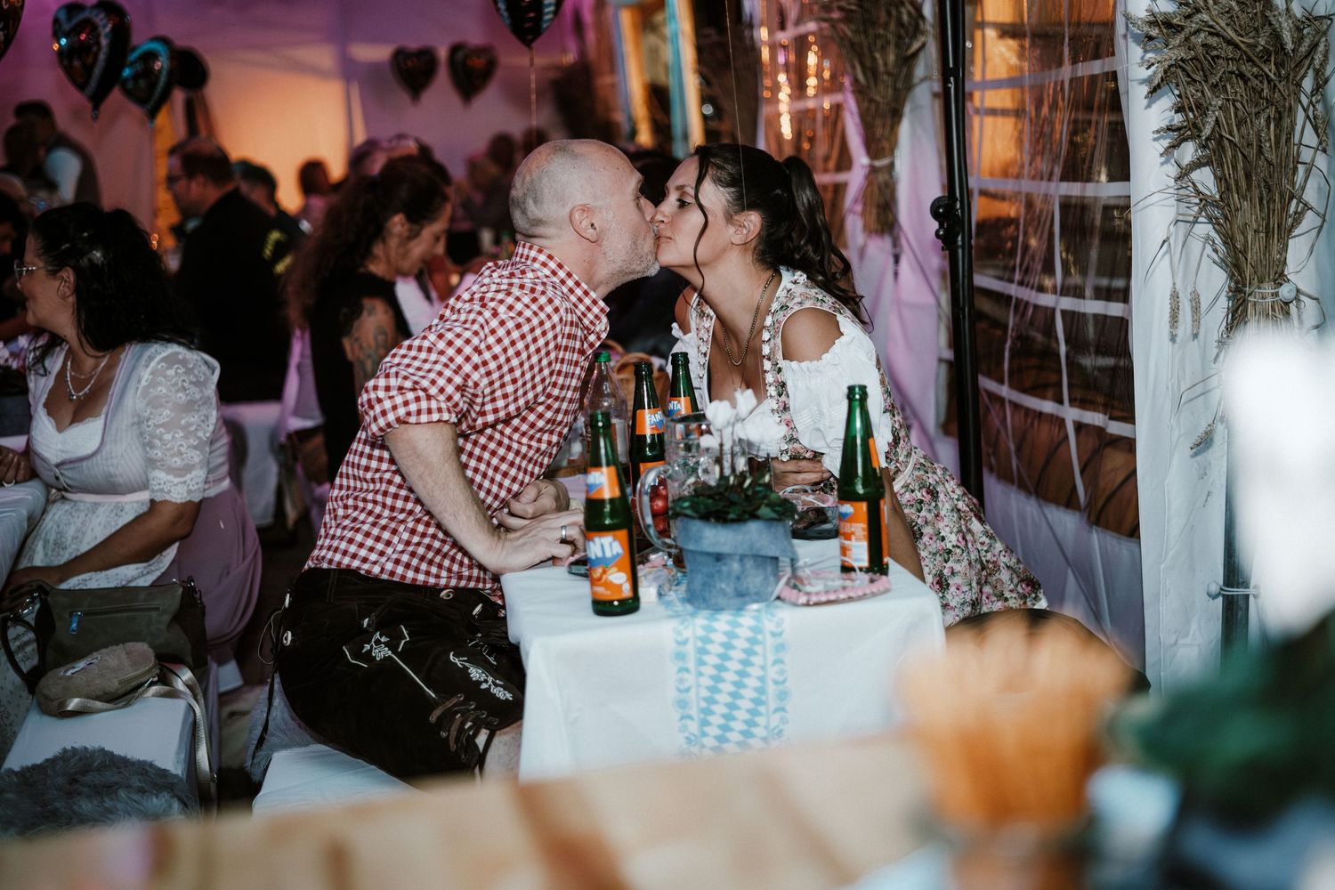 Guests enjoying a lively celebration at a restaurant with string lights and decorative hearts hanging overhead.