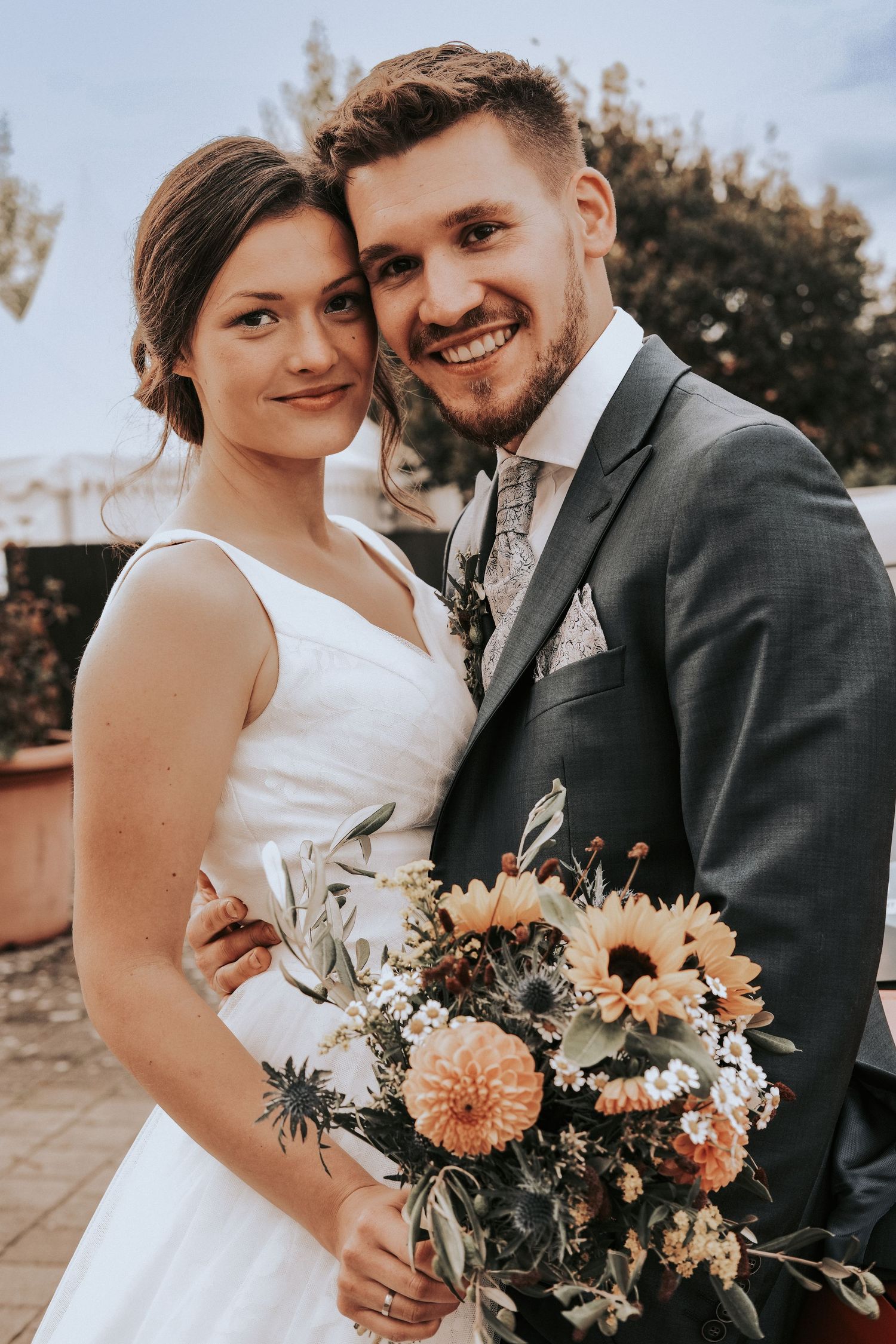Wedding couple shares intimate moments in outdoor setting with peach and white floral bouquet.