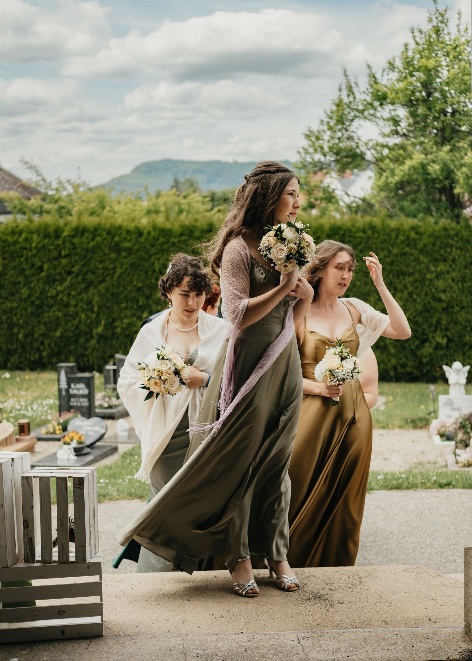 Wedding party members in brown dresses running playfully outdoors on a cloudy day.