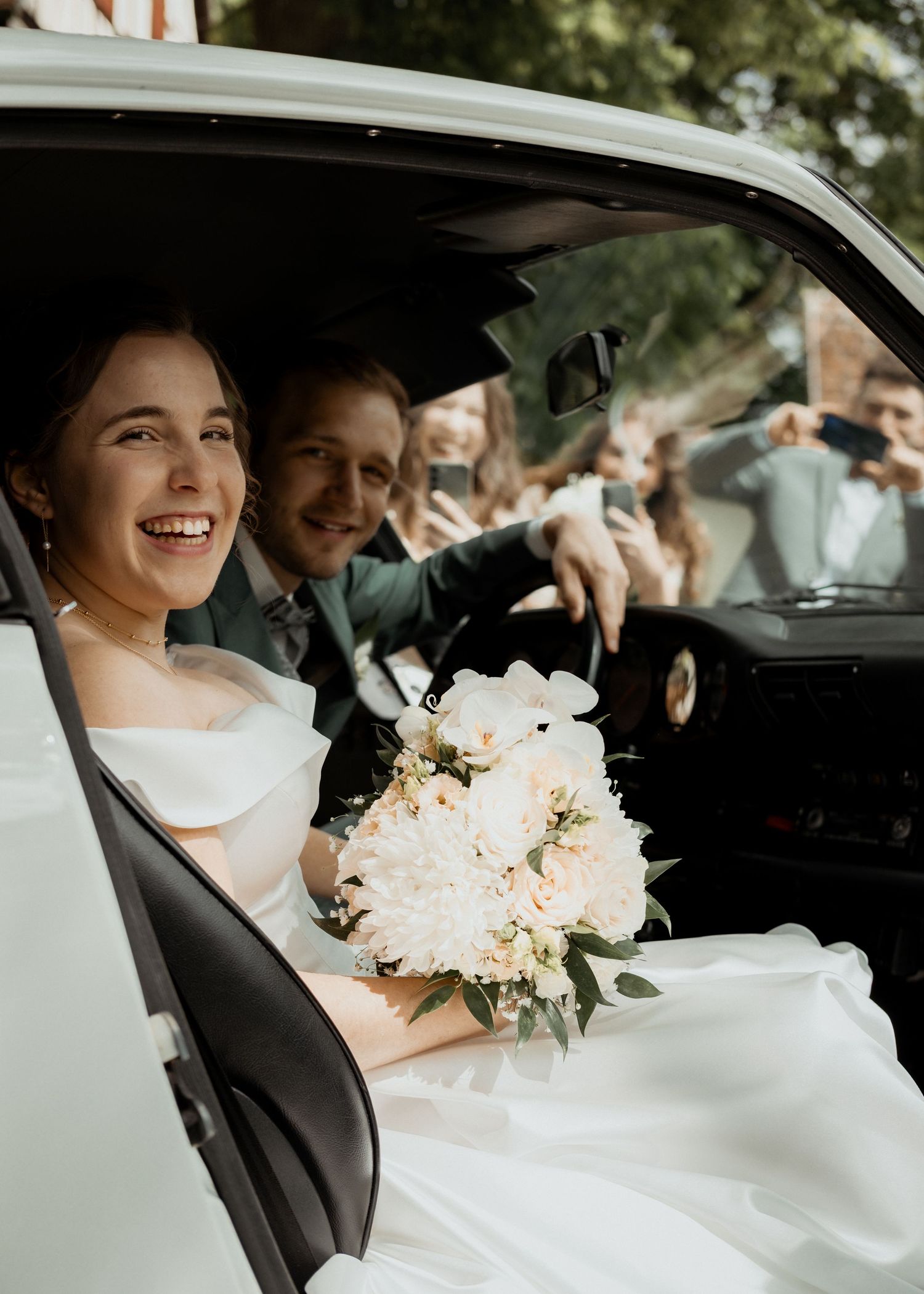 A wedding couple sitting in a car with white flowers and elegant attire.