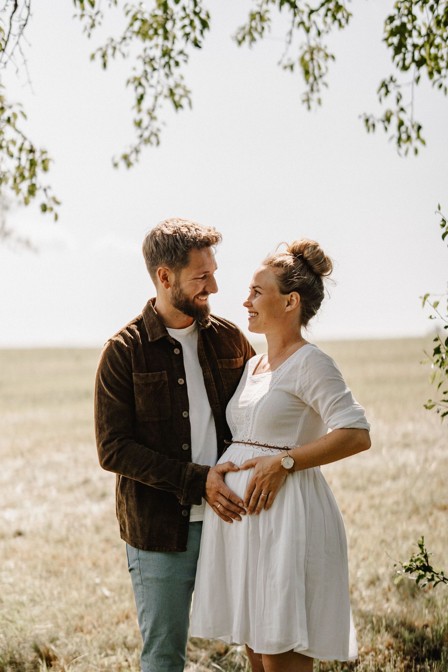 A couple shares an intimate moment together in a sunny outdoor setting with trees in the background.