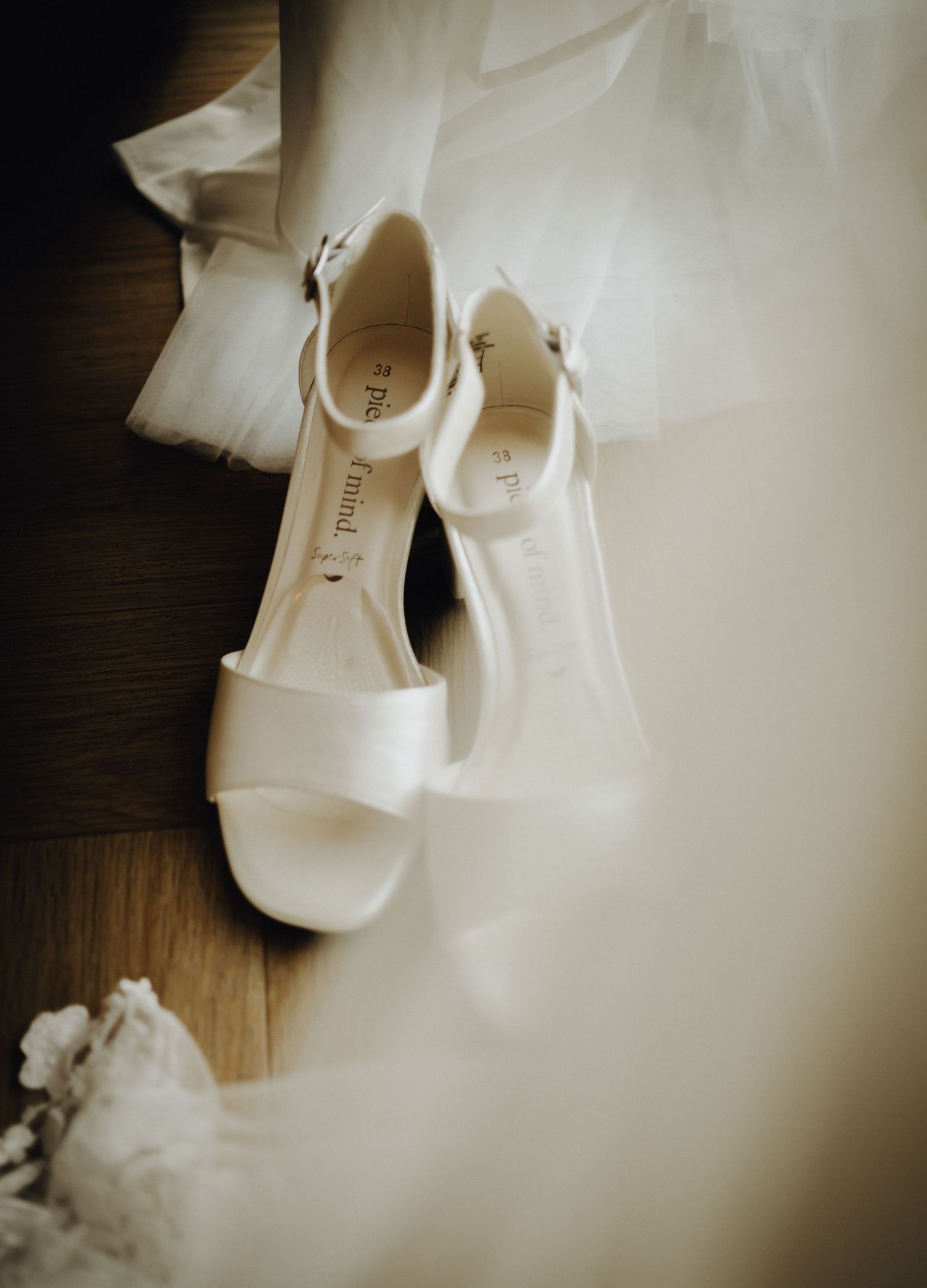 Small white baby shoes and delicate floral decorations arranged on a dark wooden surface in soft focus.