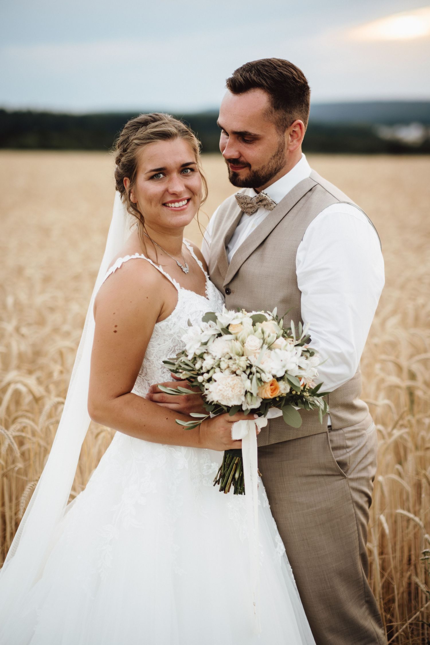 A romantic wedding couple embraces in a golden wheat field during sunset.