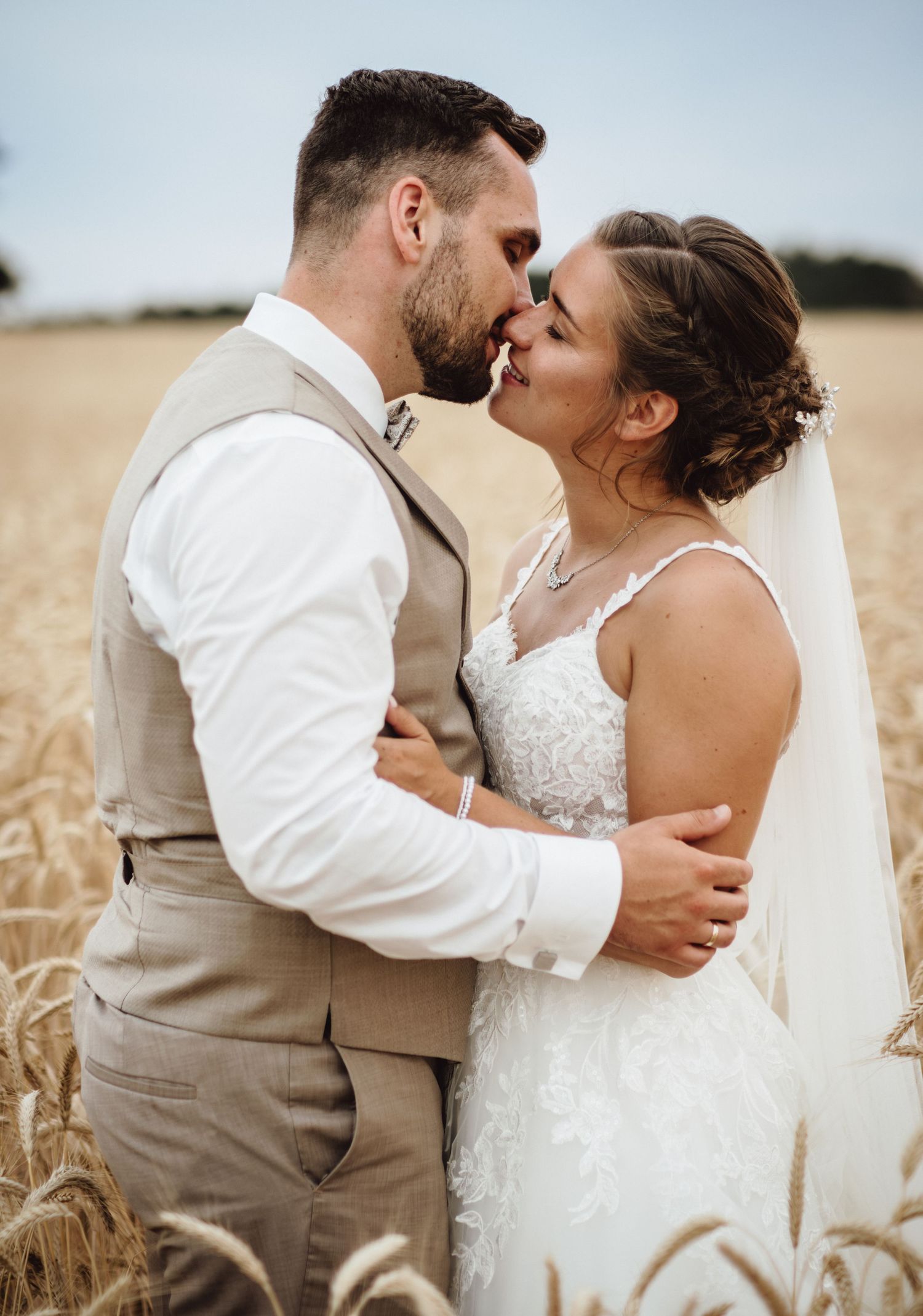 Romantic wedding couple embraces in golden wheat field during summer sunset photo session.
