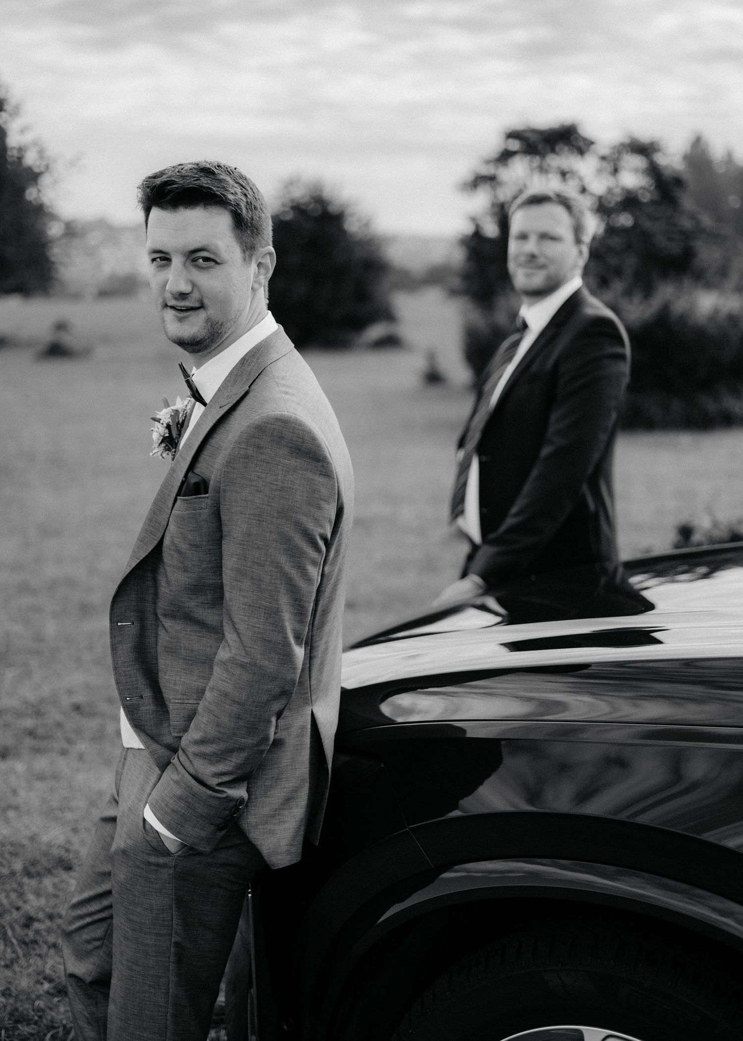 A series of black and white photos showing a person in a gray suit leaning against a black car in an outdoor setting.