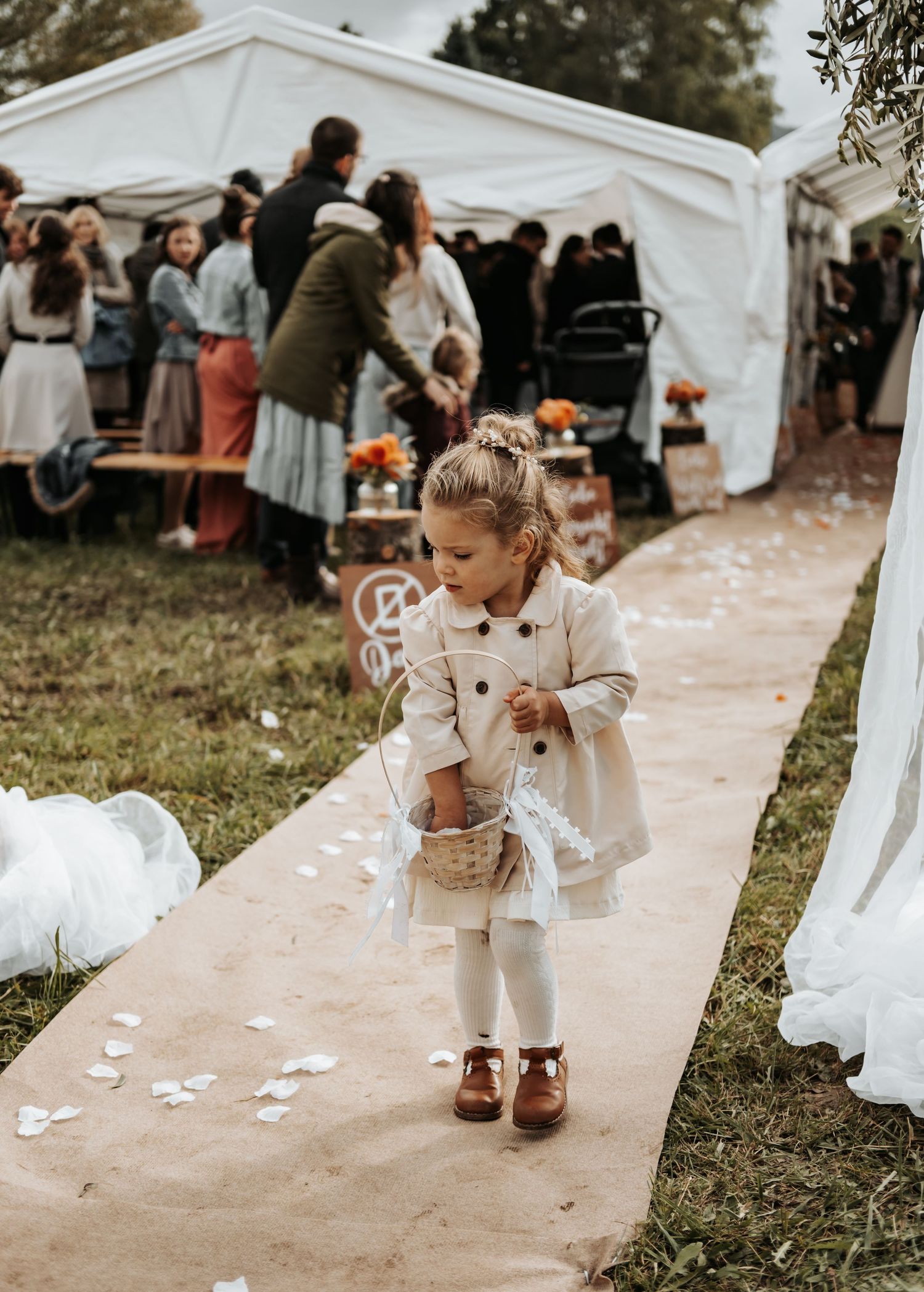 A sequence of four images shows a small child in white playing with flower petals on a paved walkway at an outdoor event.