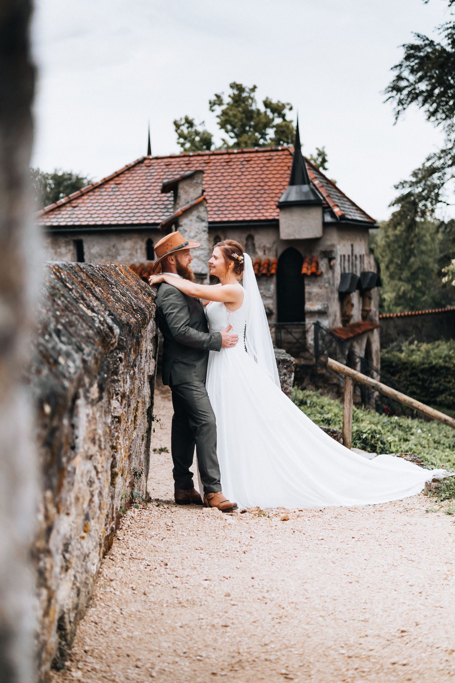 A couple in wedding attire share a romantic dance together on a stone path near rustic buildings.
