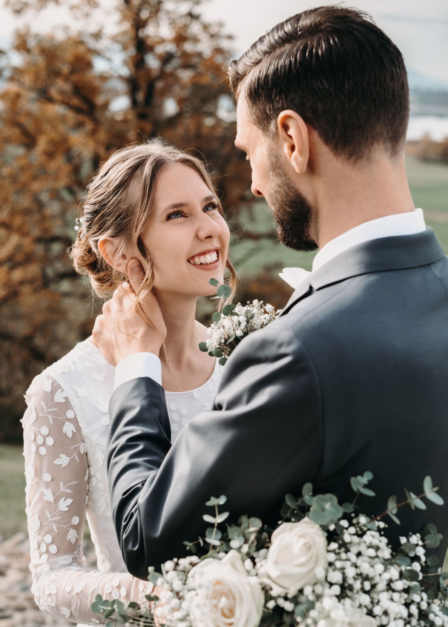 A romantic wedding couple shares intimate moments against an autumn backdrop with delicate white flowers and elegant attire.