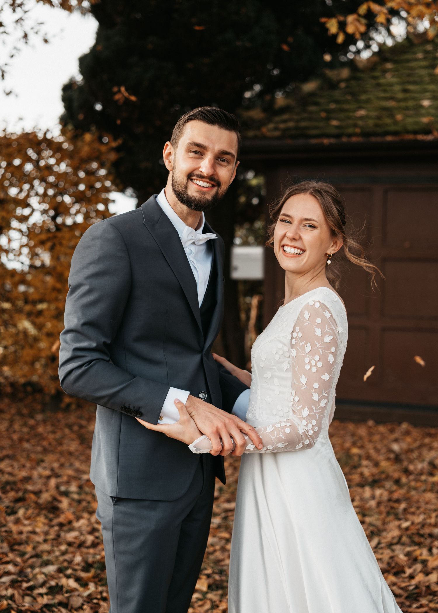 A couple shares joyful moments in autumn leaves wearing wedding attire during their outdoor photoshoot.