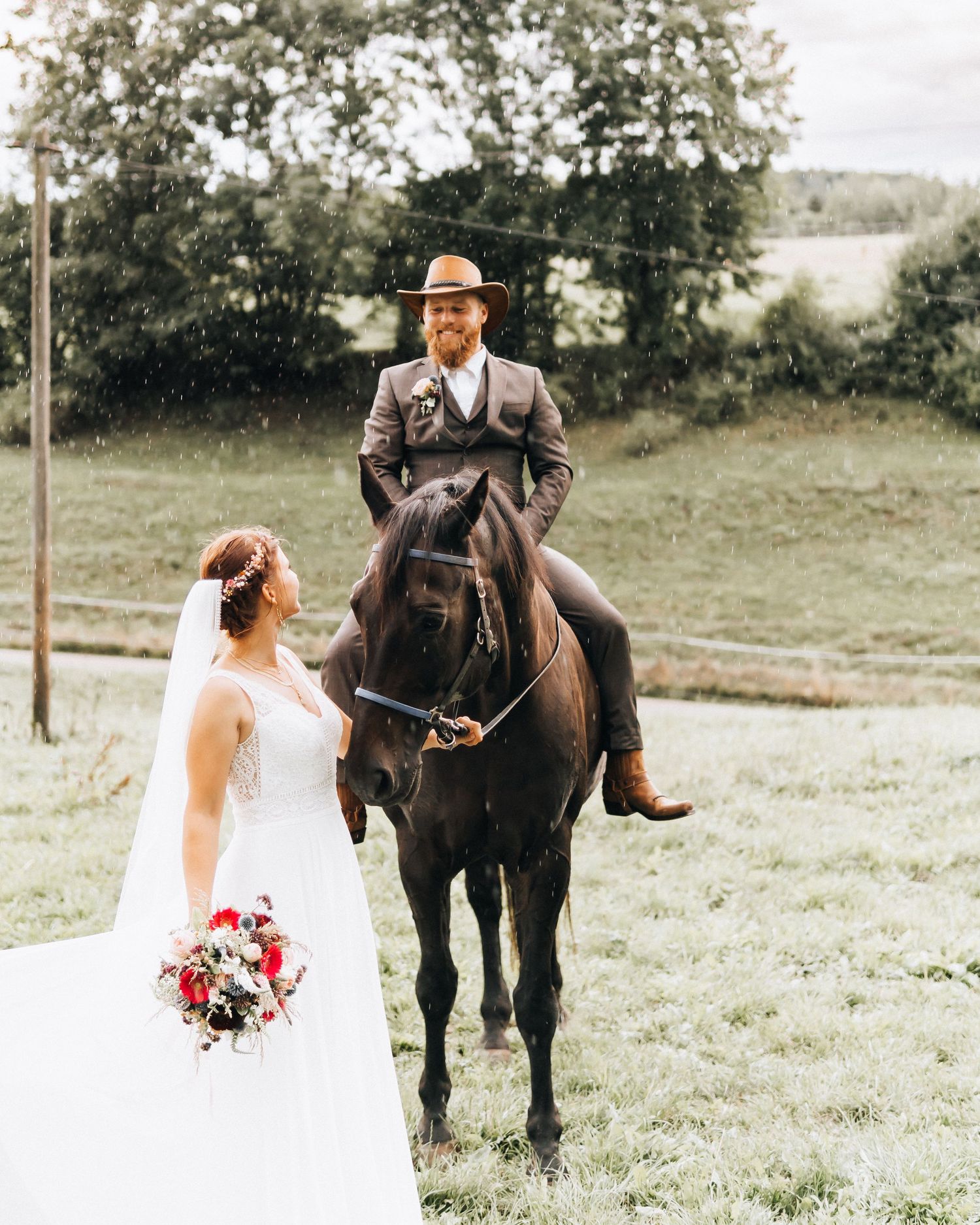 A romantic wedding scene in a meadow with a dark horse and floral bouquet against a rustic countryside backdrop.