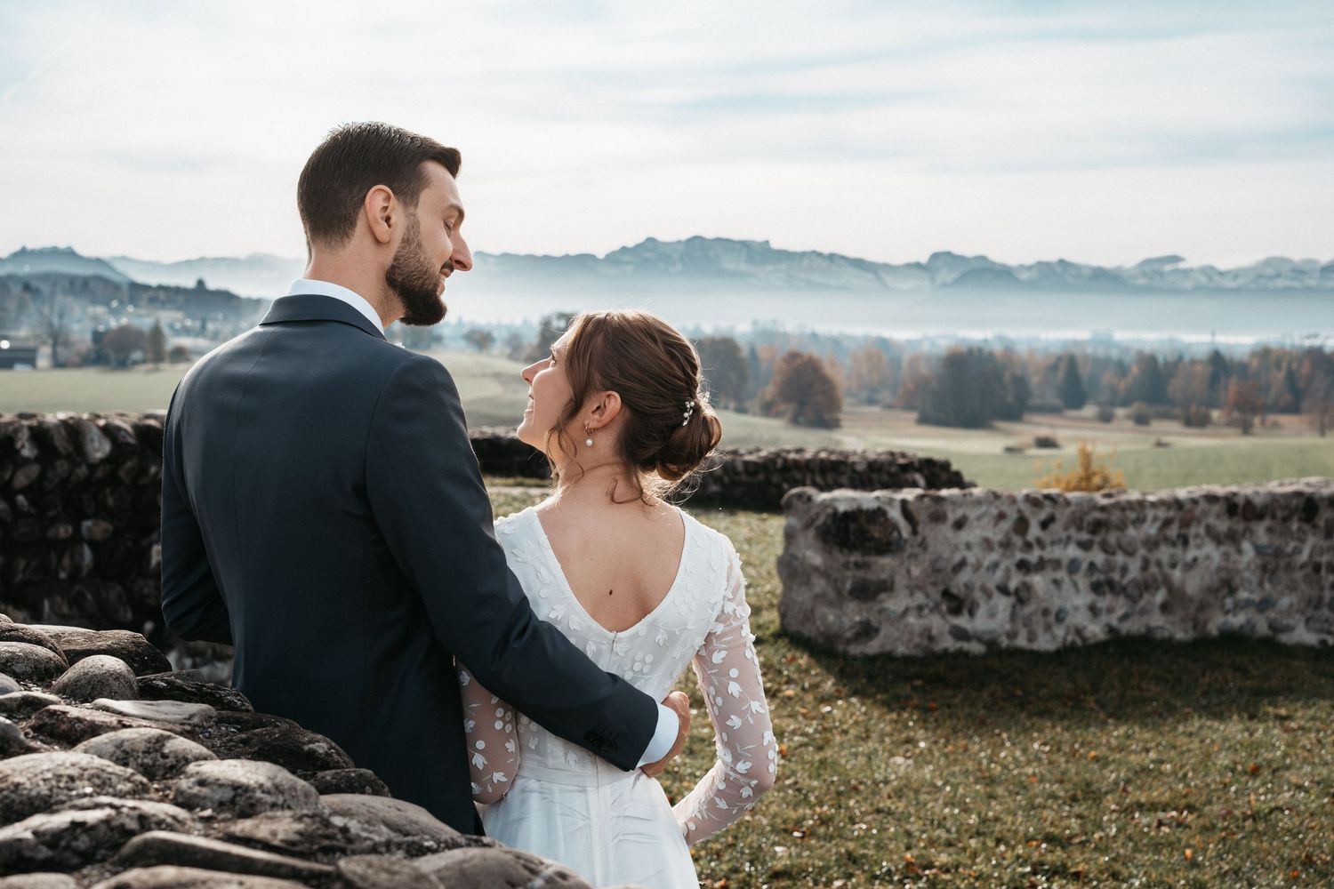 Newlywed couple embraces while overlooking scenic mountain landscape during outdoor wedding photo session.