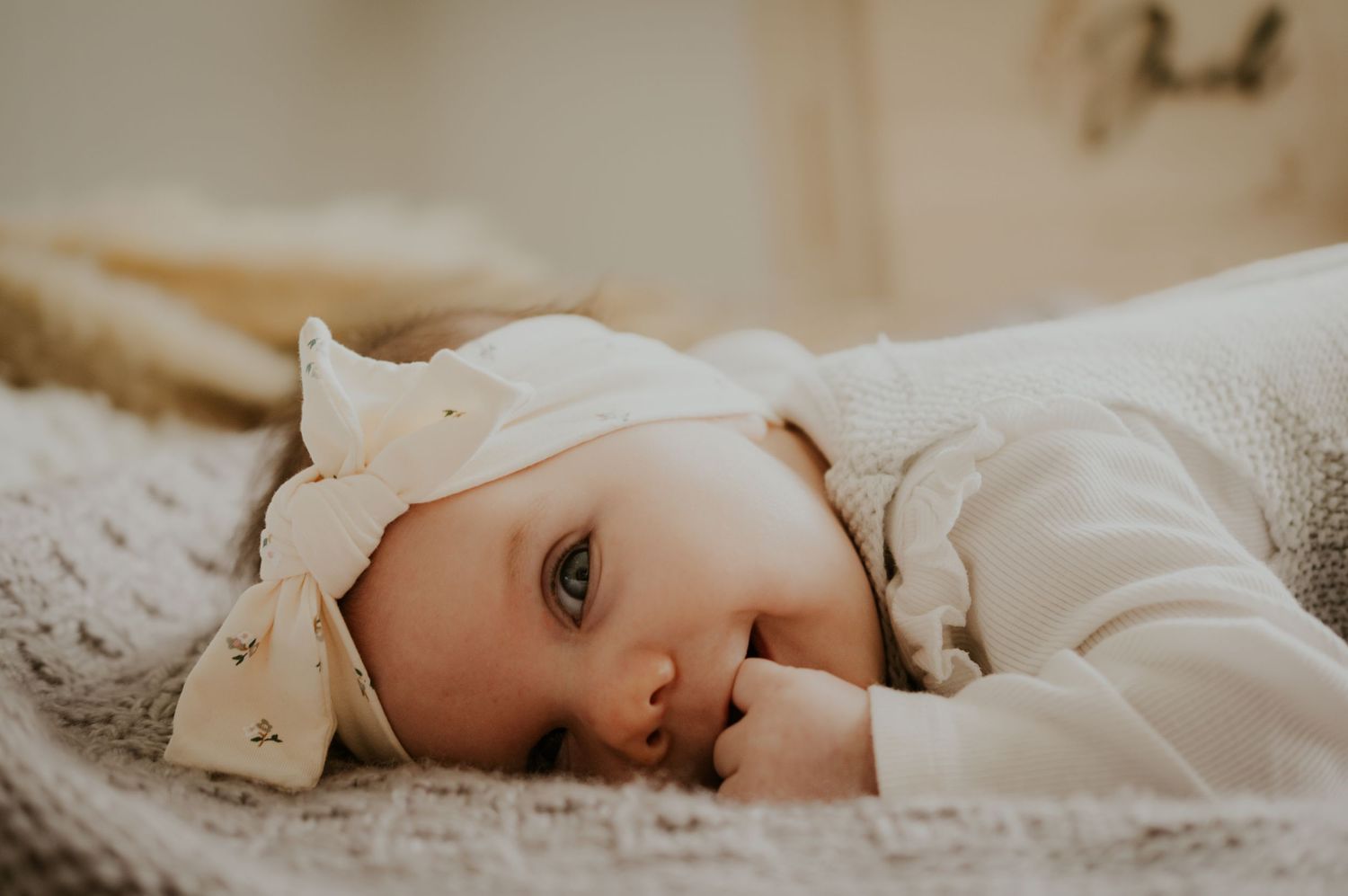 Baby lying on white bedding in soft natural light creates peaceful nursery scene.