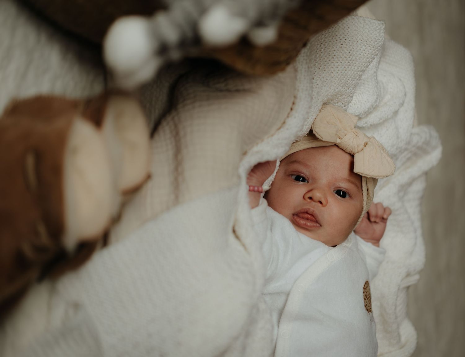 A baby wearing a white bonnet and swaddled in soft white fabric lies peacefully in bed.