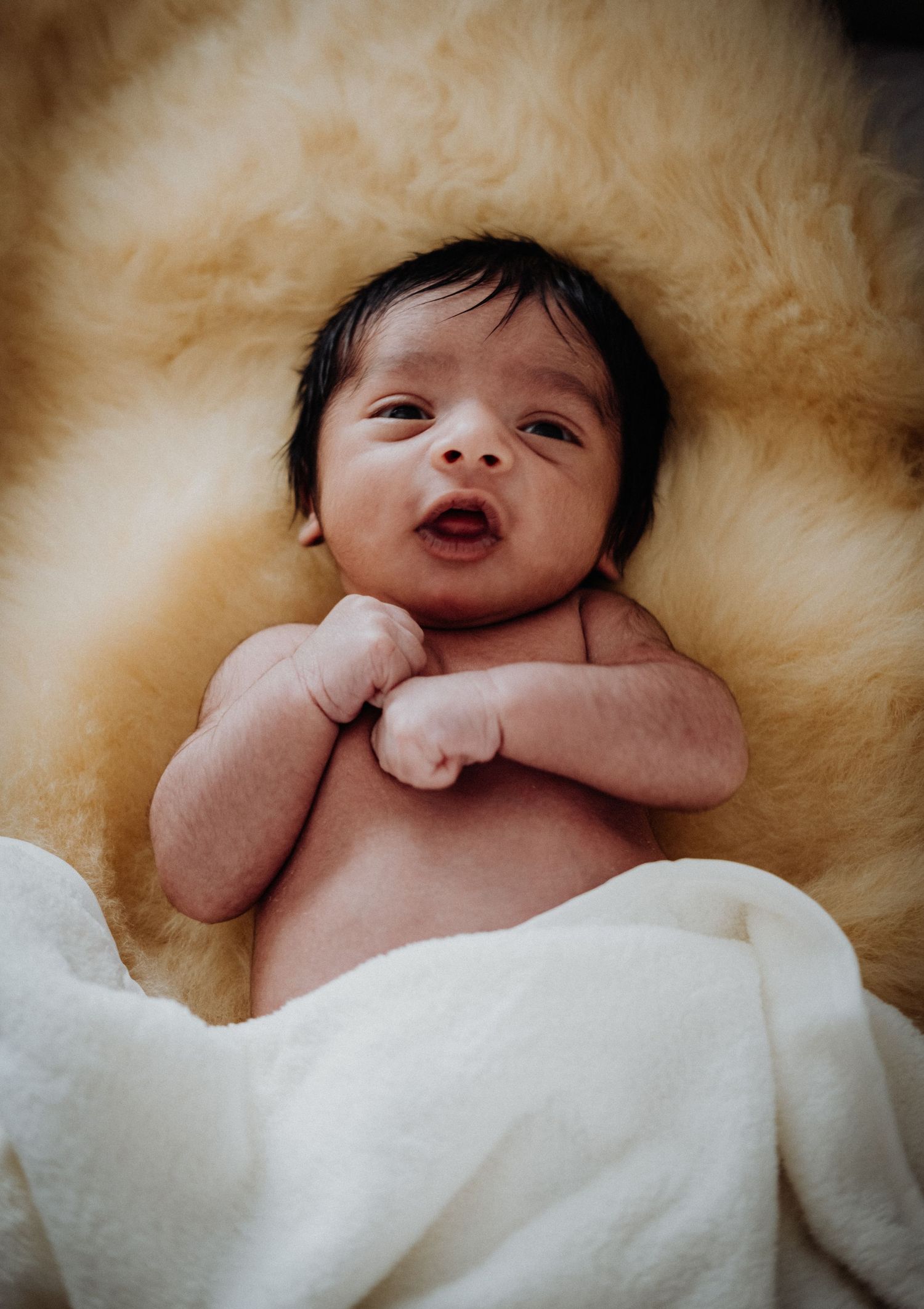 A newborn baby lying on soft white sheepskin bedding in a series of peaceful sleeping poses.