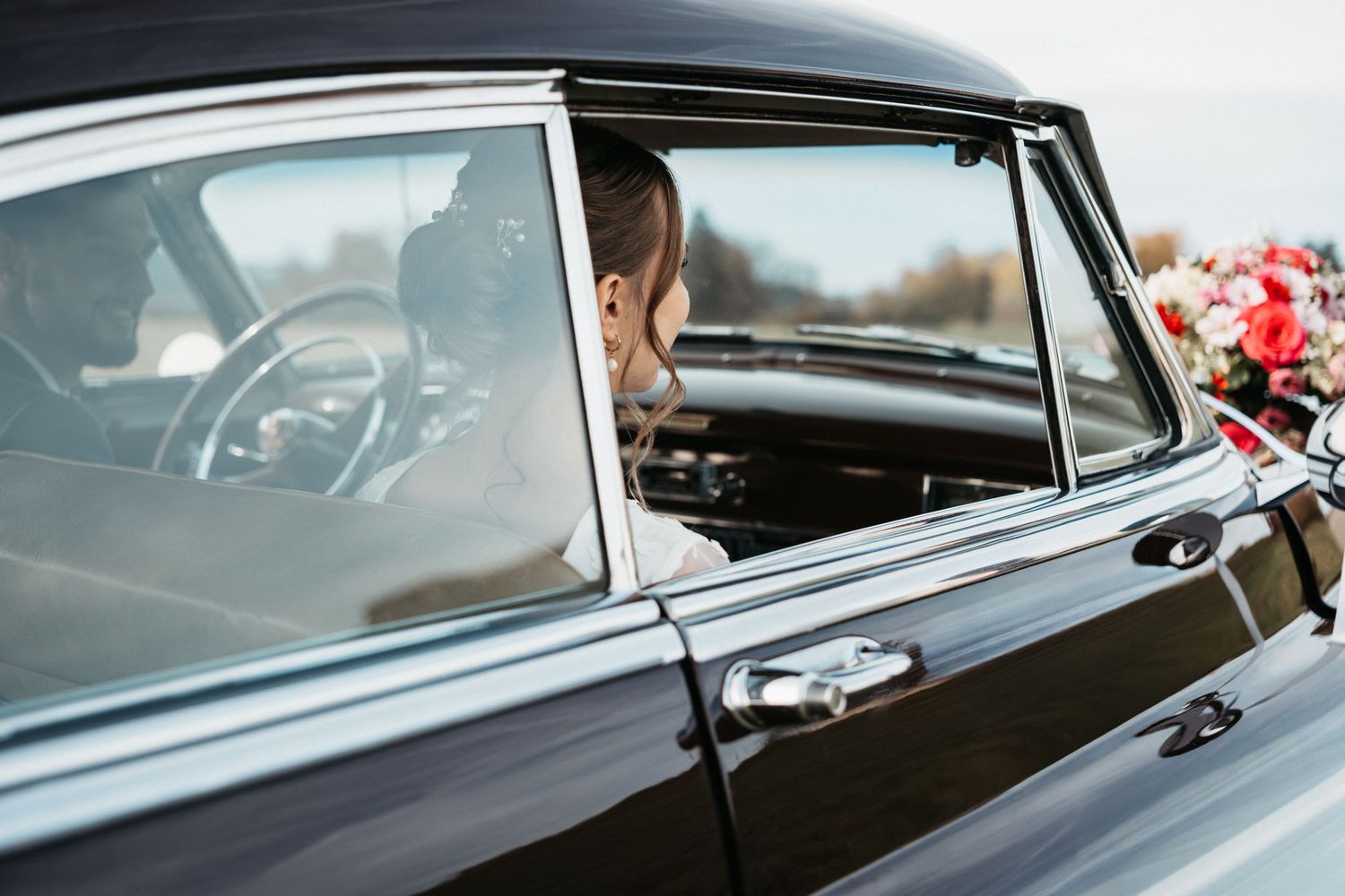 Close-up view of a black classic car's side panel showing sleek chrome trim and window details.