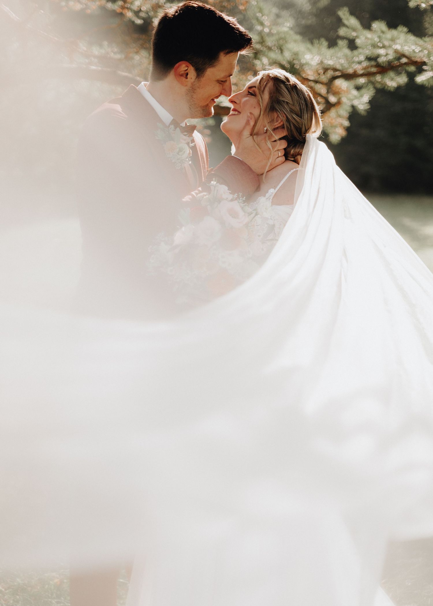 A romantic couple shares an intimate moment in an ethereal outdoor setting with soft white flowing fabric creating a dreamy atmosphere.