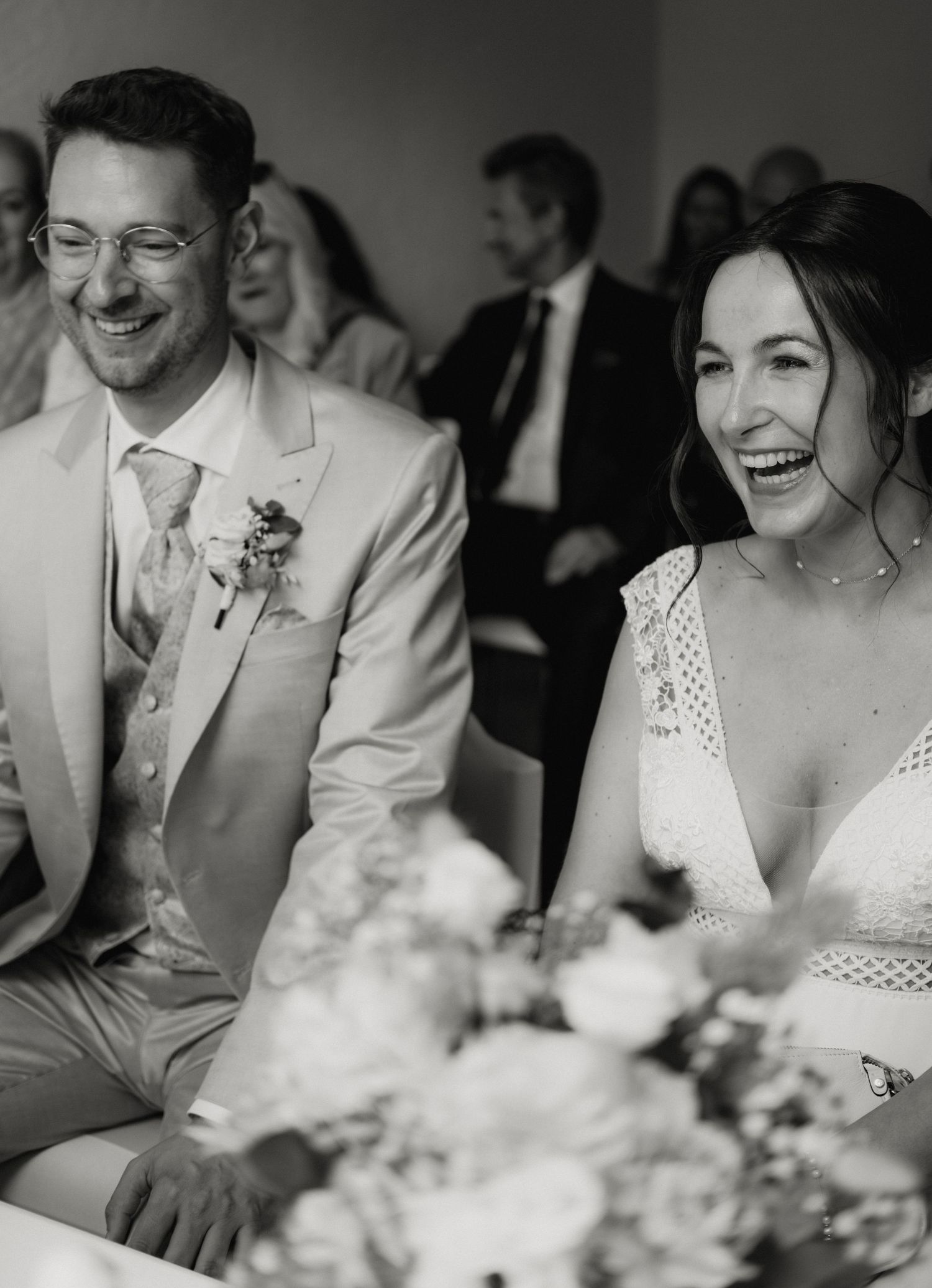 Black and white candid photos show joyful laughter and genuine moments between wedding guests during a reception.