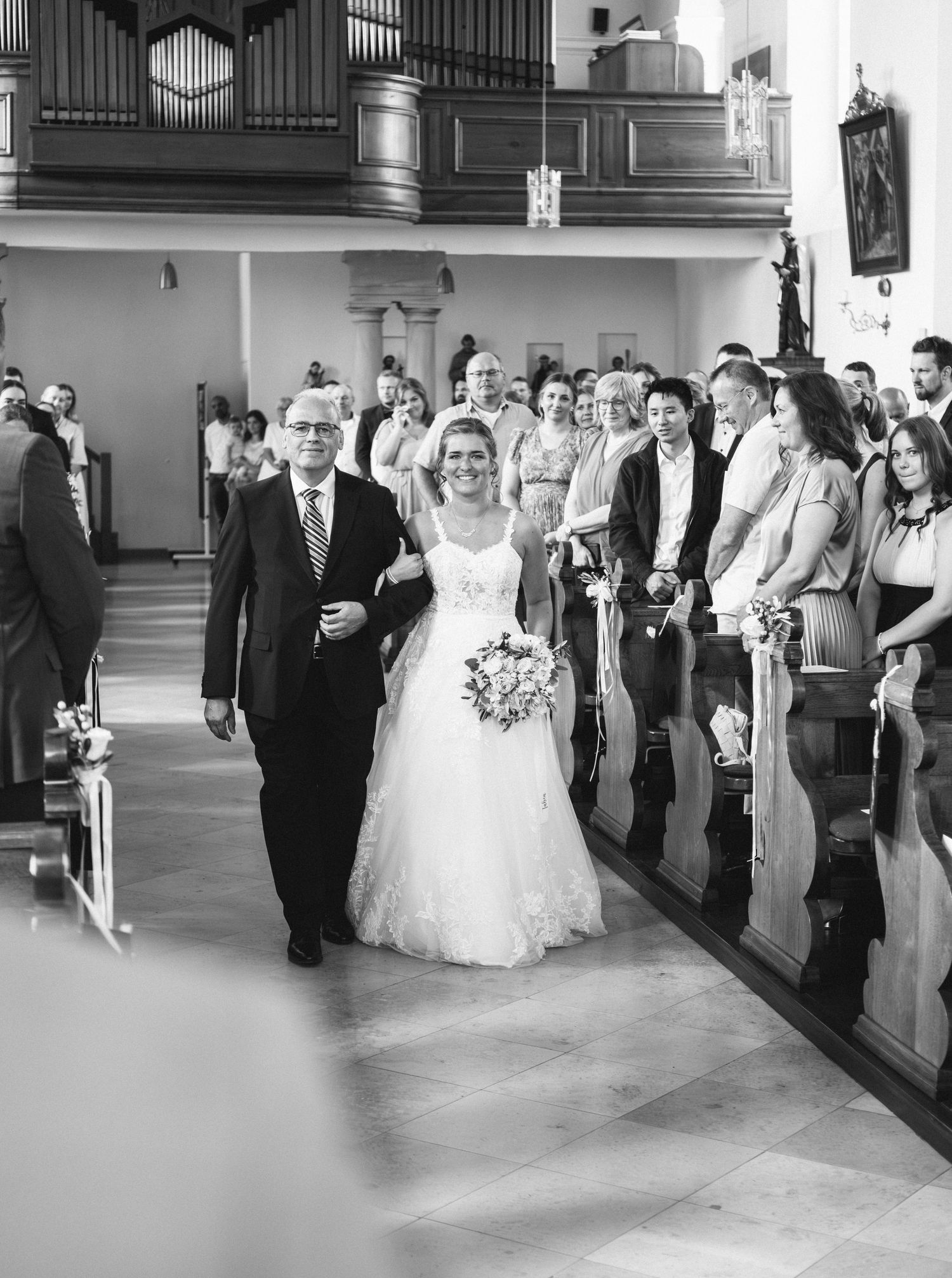 A black and white photograph showing a traditional church wedding processional down the center aisle.