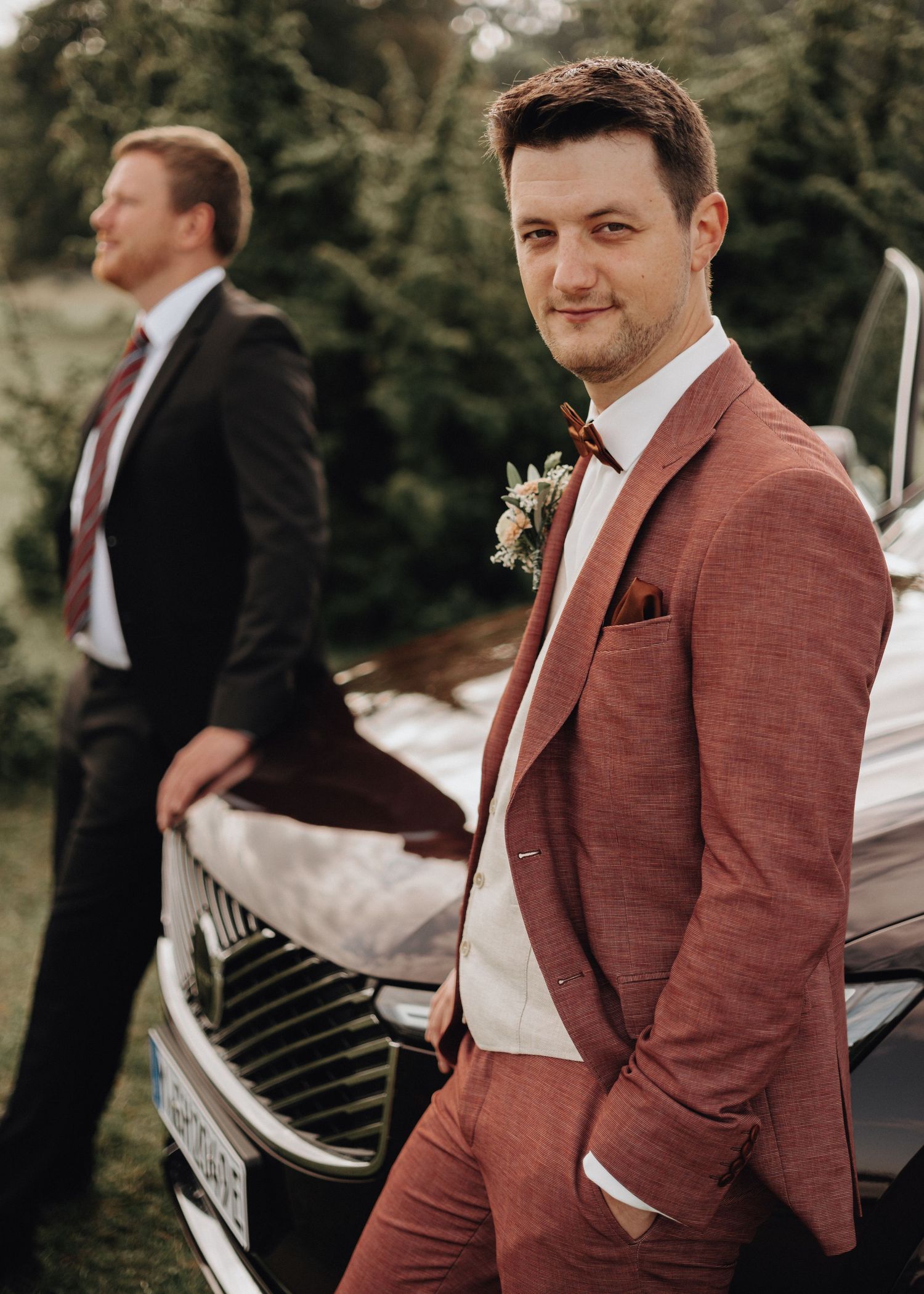 Groomsmen in burgundy suits and black ties pose playfully by a piano during a wedding celebration.