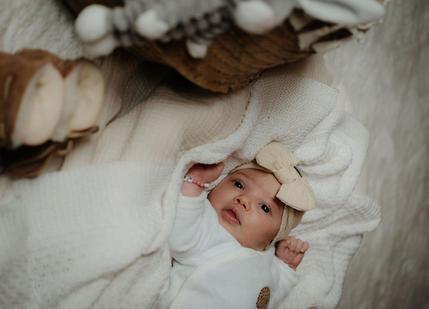 Newborn baby wrapped in white blanket lies peacefully while being photographed in natural light.