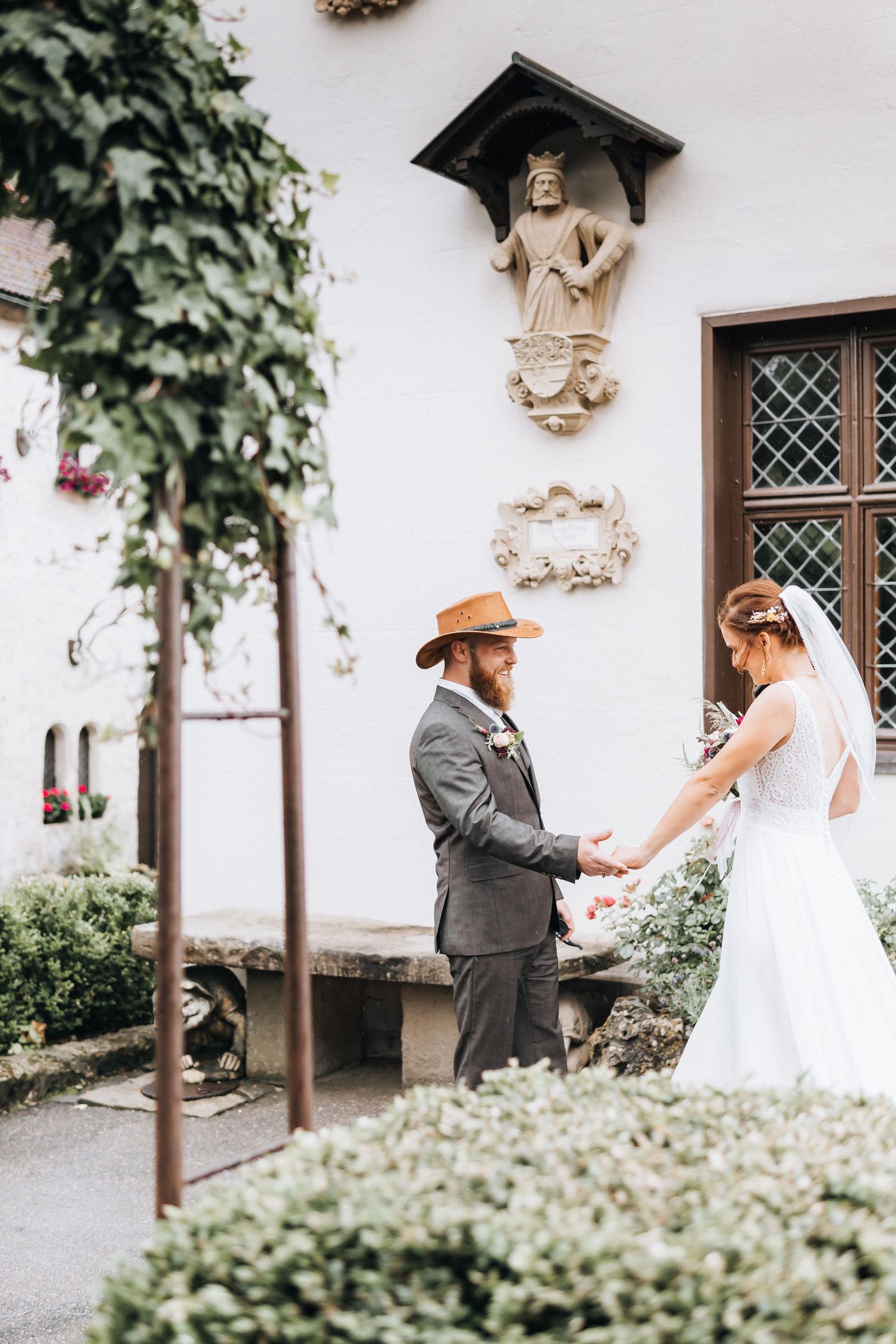 A couple shares an intimate first look moment outside a white church with ornate architectural details and climbing vines.