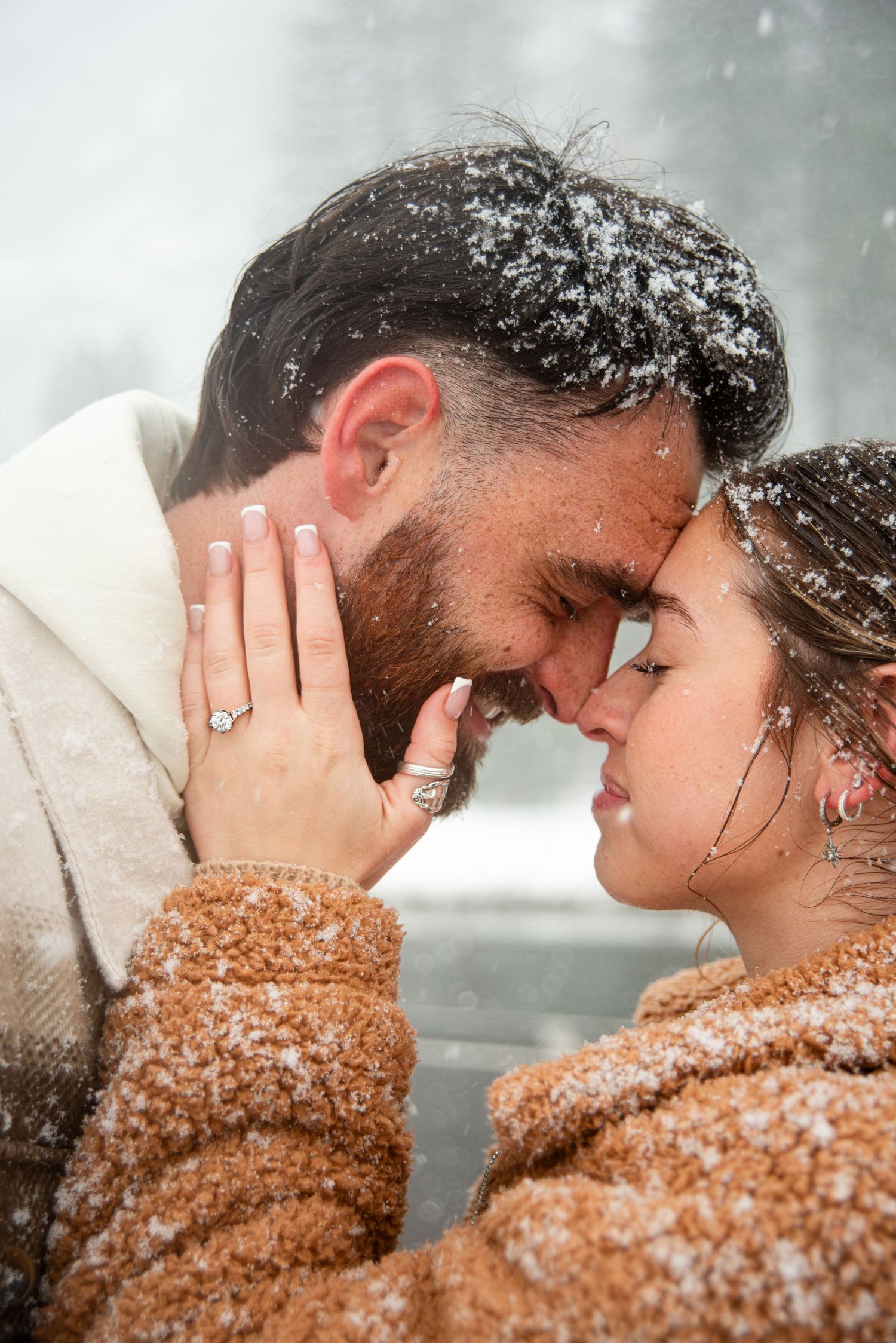 A romantic close-up moment captured in falling snow with warm brown tones.