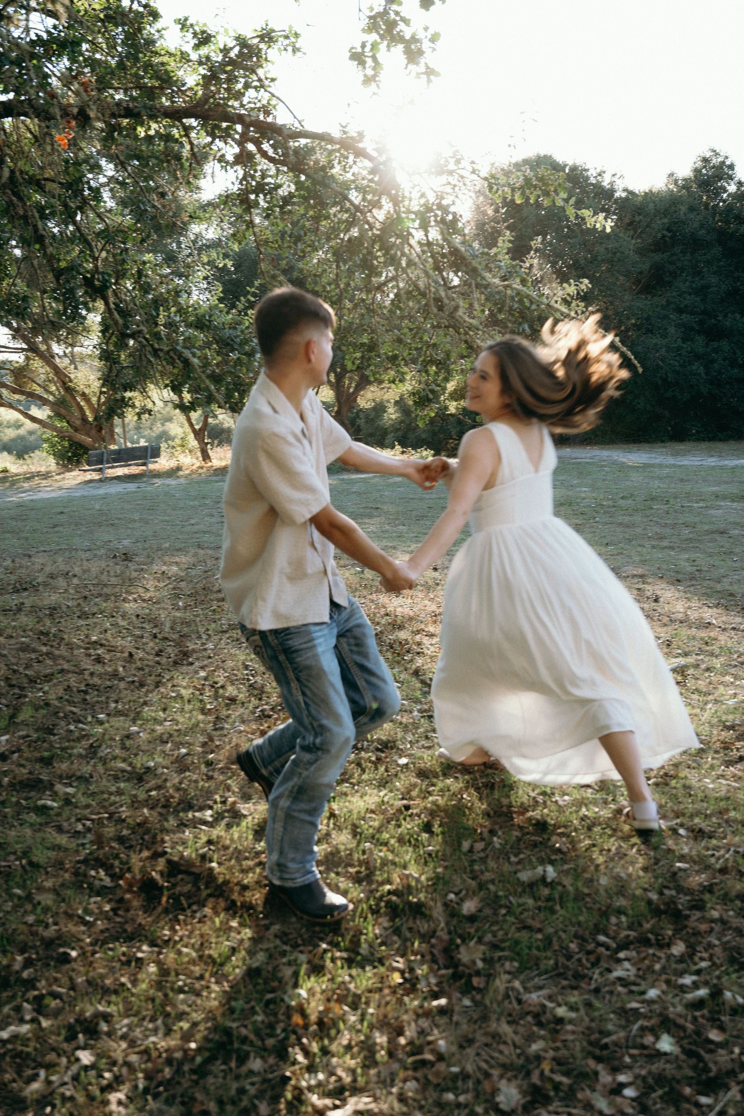 Couple in white and denim dancing playfully outdoors on fallen leaves.
