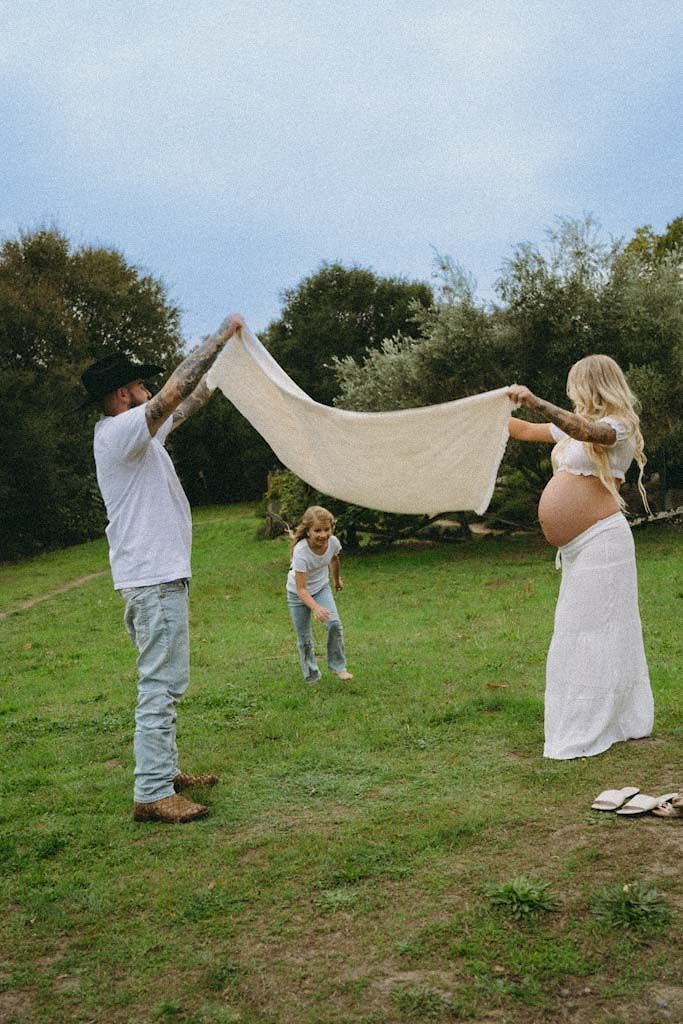 A family plays with a white sheet outdoors on a grassy hillside.