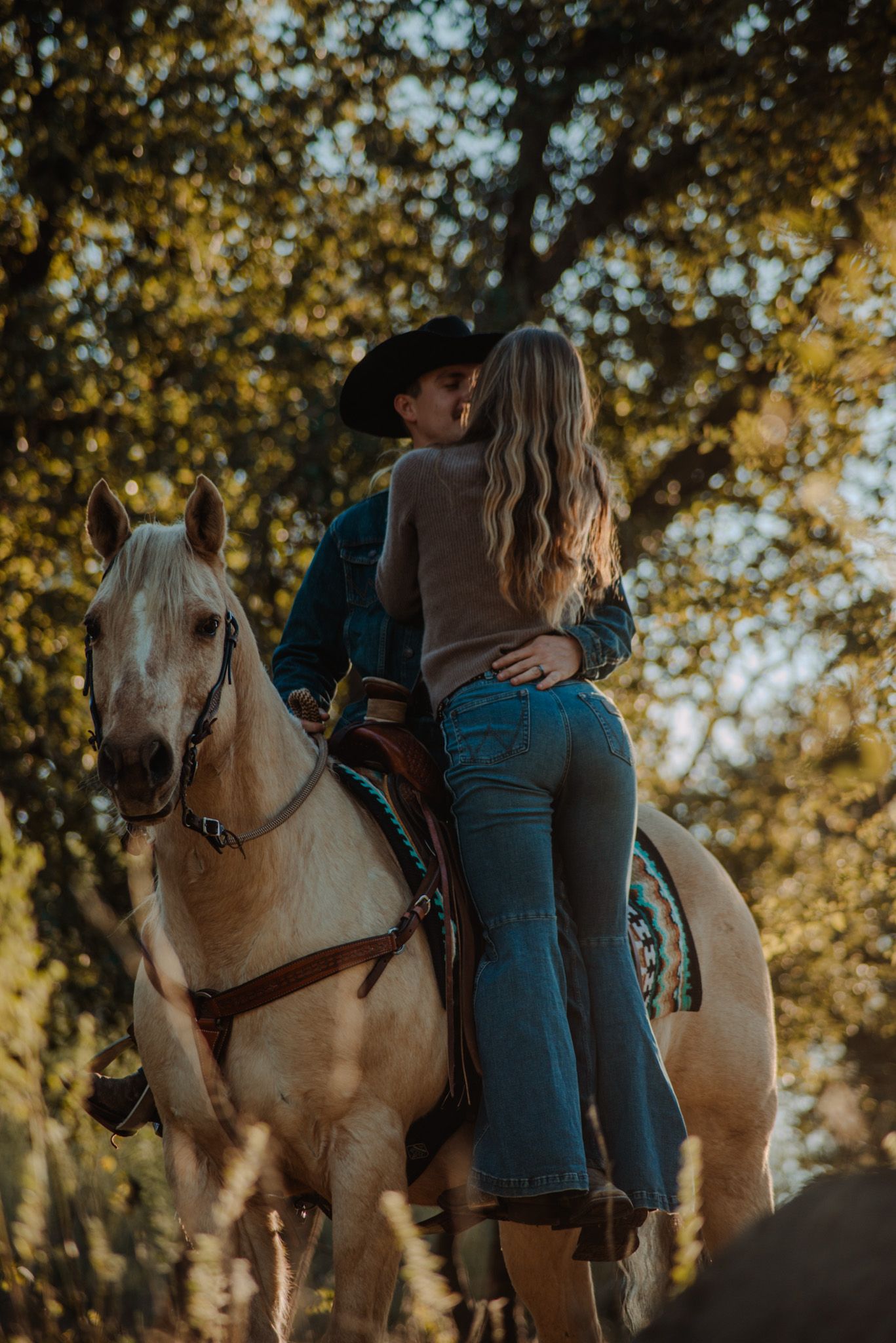 A couple rides together on a white horse during golden hour in an autumn setting.
