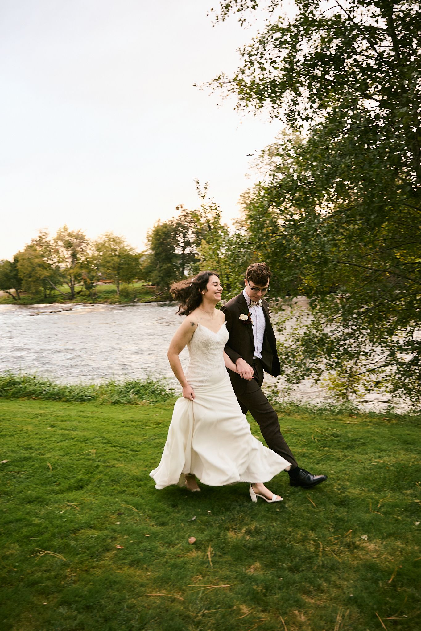 A couple dances and plays together on a grassy lawn at sunset near a lake.