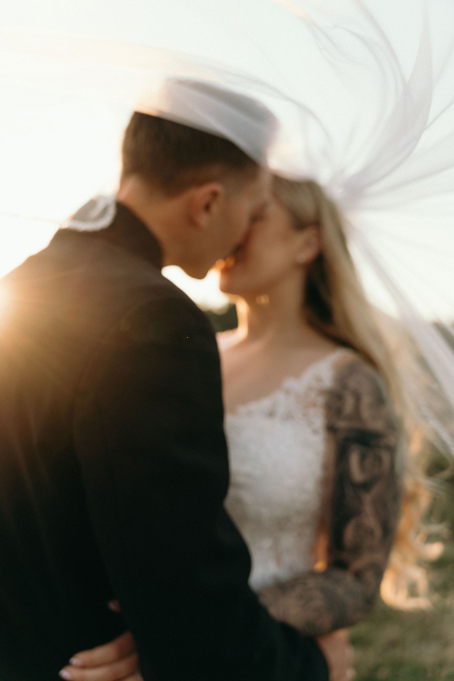 Romantic silhouette of newlyweds embracing during sunset with bride's veil flowing in the wind.