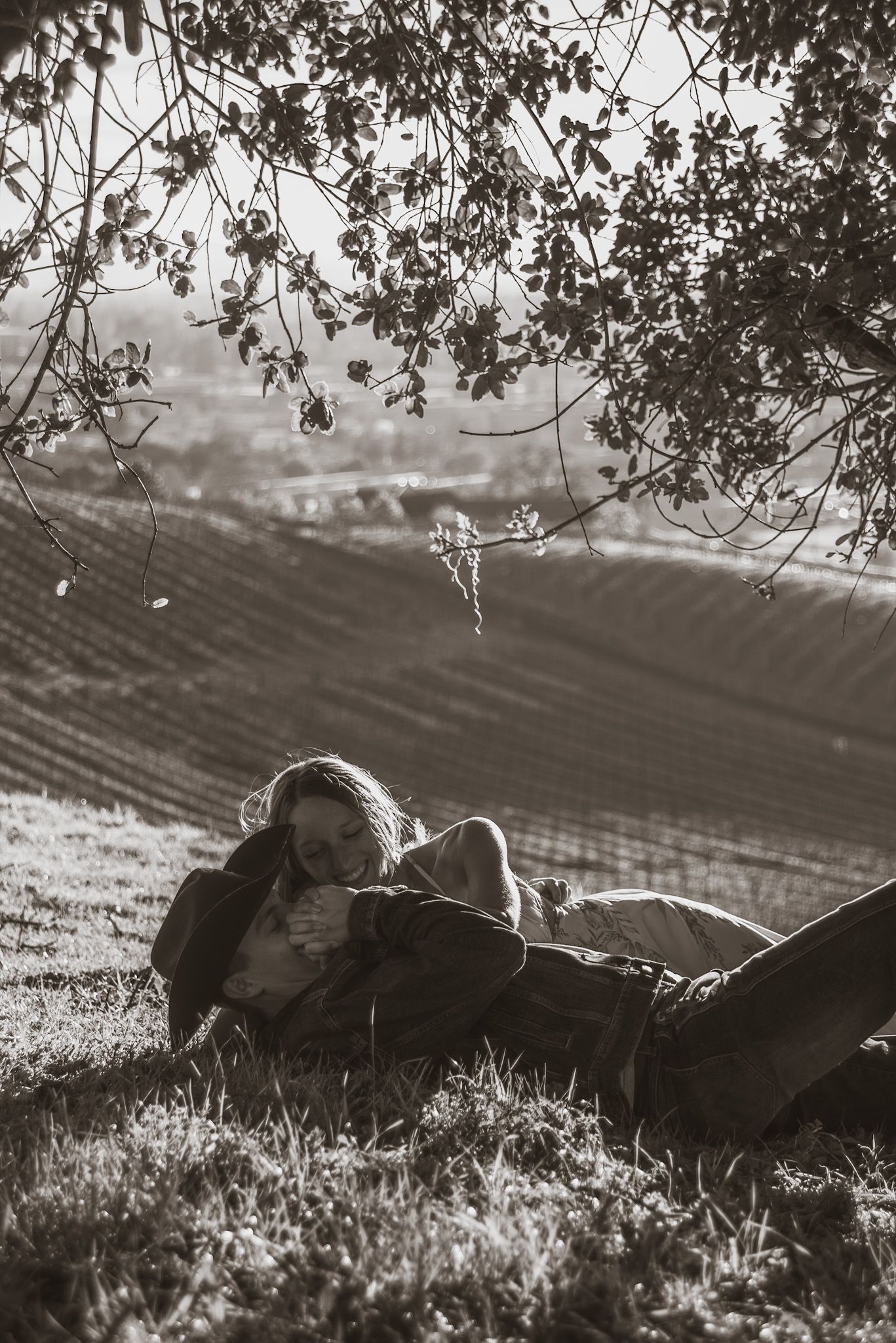 A couple relaxes under a tree during sunset in a black and white countryside scene.