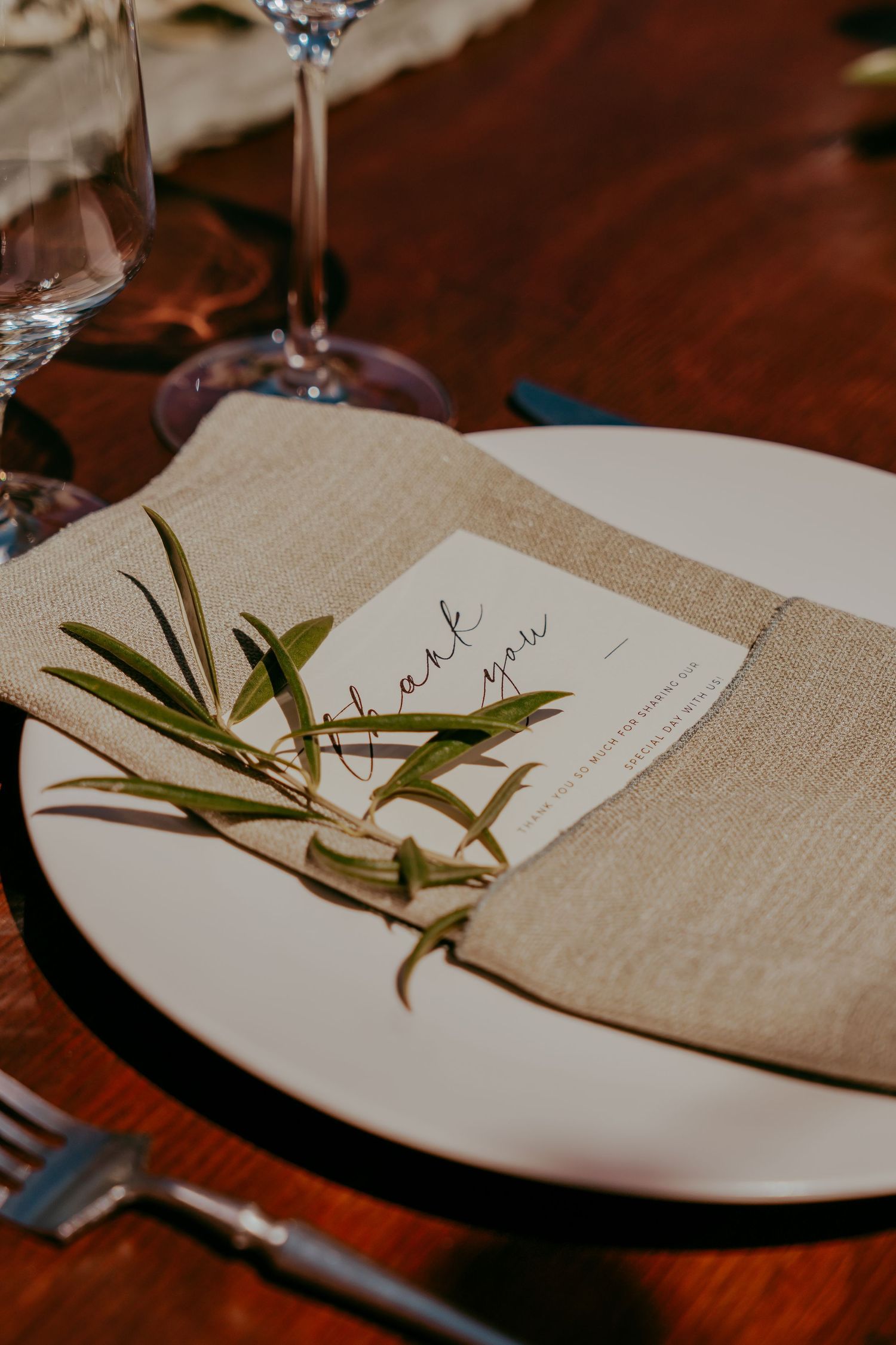 Place setting with linen napkin and greenery sprig on white plate at elegant table.
