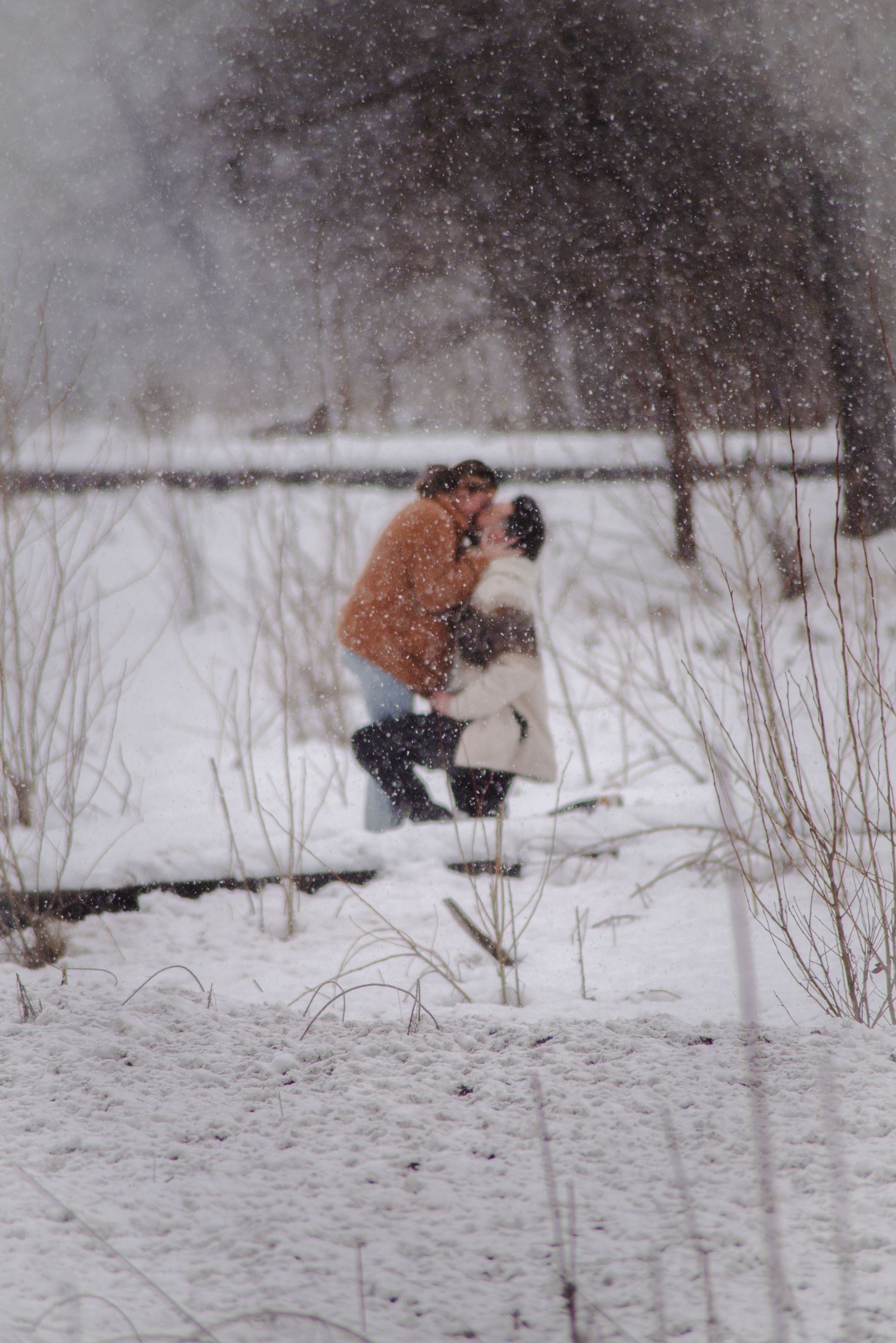 A couple shares an intimate moment while kneeling in fresh snow during winter.