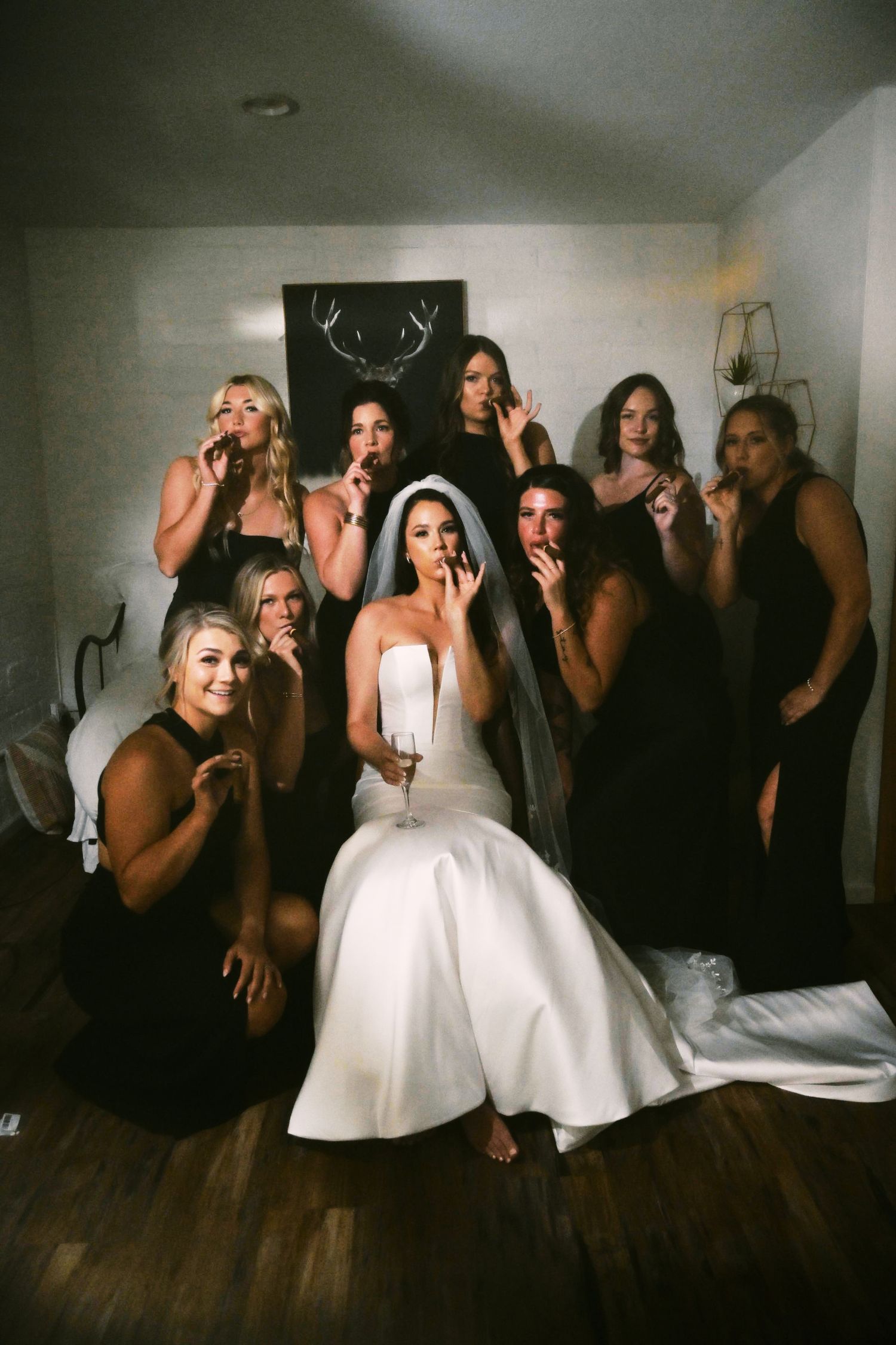 Bride in white gown and veil poses with bridesmaids in black dresses for a fun wedding party photo indoors.